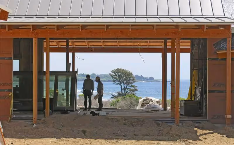 Two people view ocean through wooden frame of unfinished coastal building