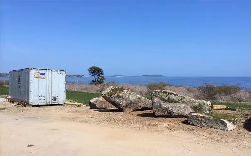 Shipping container near rocky shore with blue ocean and distant islands