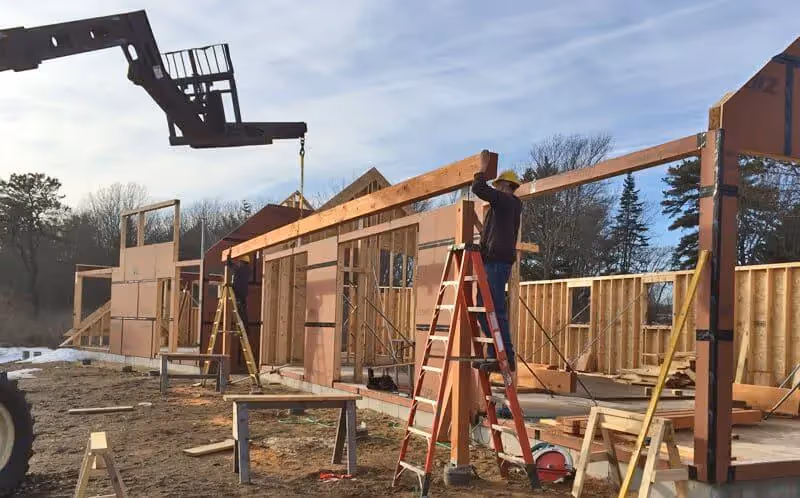 Construction workers building wooden frame house with crane and ladders