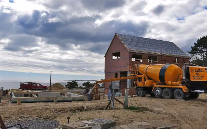 Yellow concrete mixer truck at construction site with wooden house frame