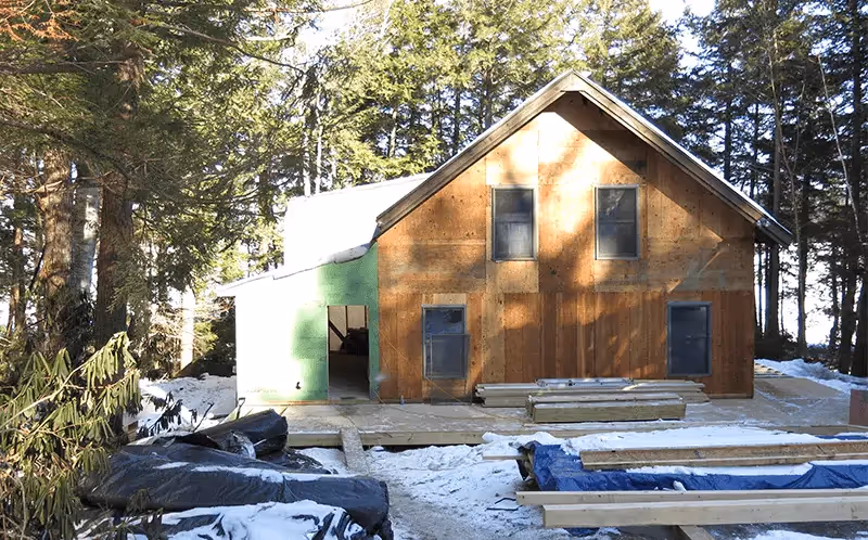 Wooden cabin with green door in snowy forest, construction materials around