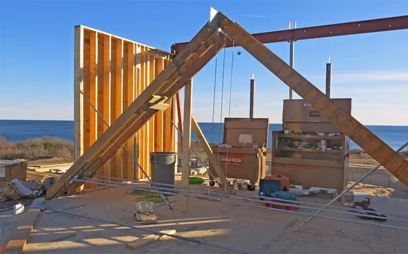 Wooden framed house under construction near ocean with construction equipment