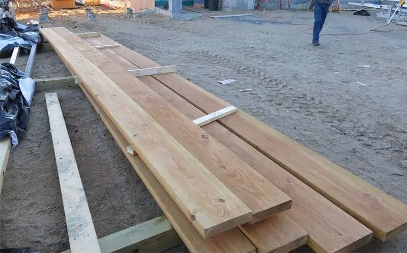 Long wooden planks stacked on construction site with sandy ground