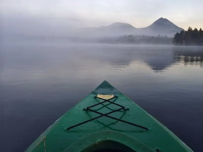 Green kayak on misty lake with mountains reflecting in calm water