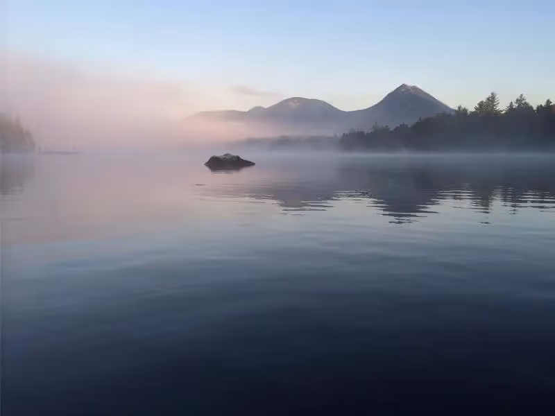 Misty mountain lake at dawn with calm water and soft pastel sky