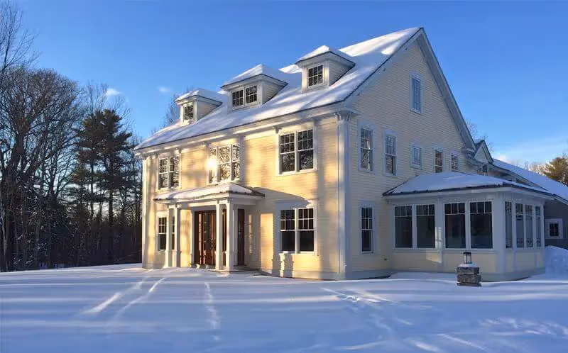 Yellow two-story house with snow-covered ground and winter trees