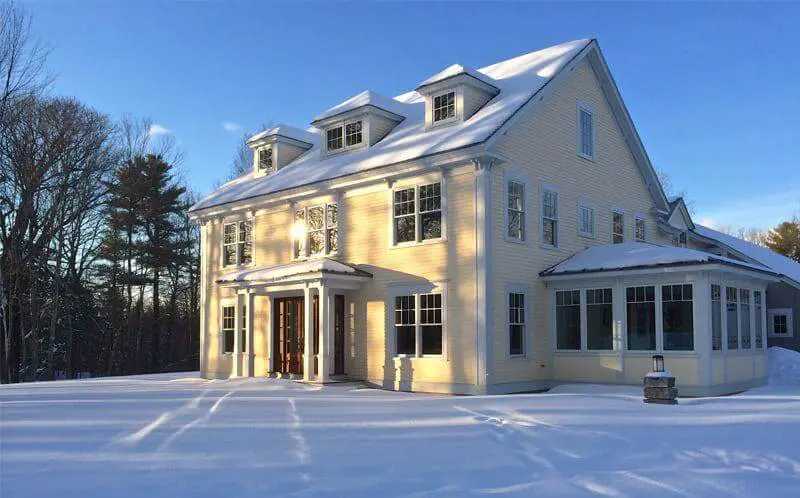 Yellow two-story house with snow-covered ground and winter trees