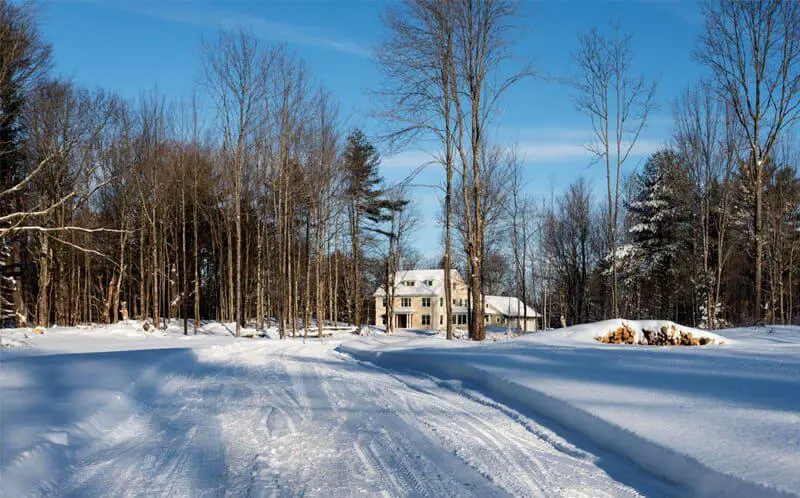 Snowy winter landscape with white house nestled among bare trees