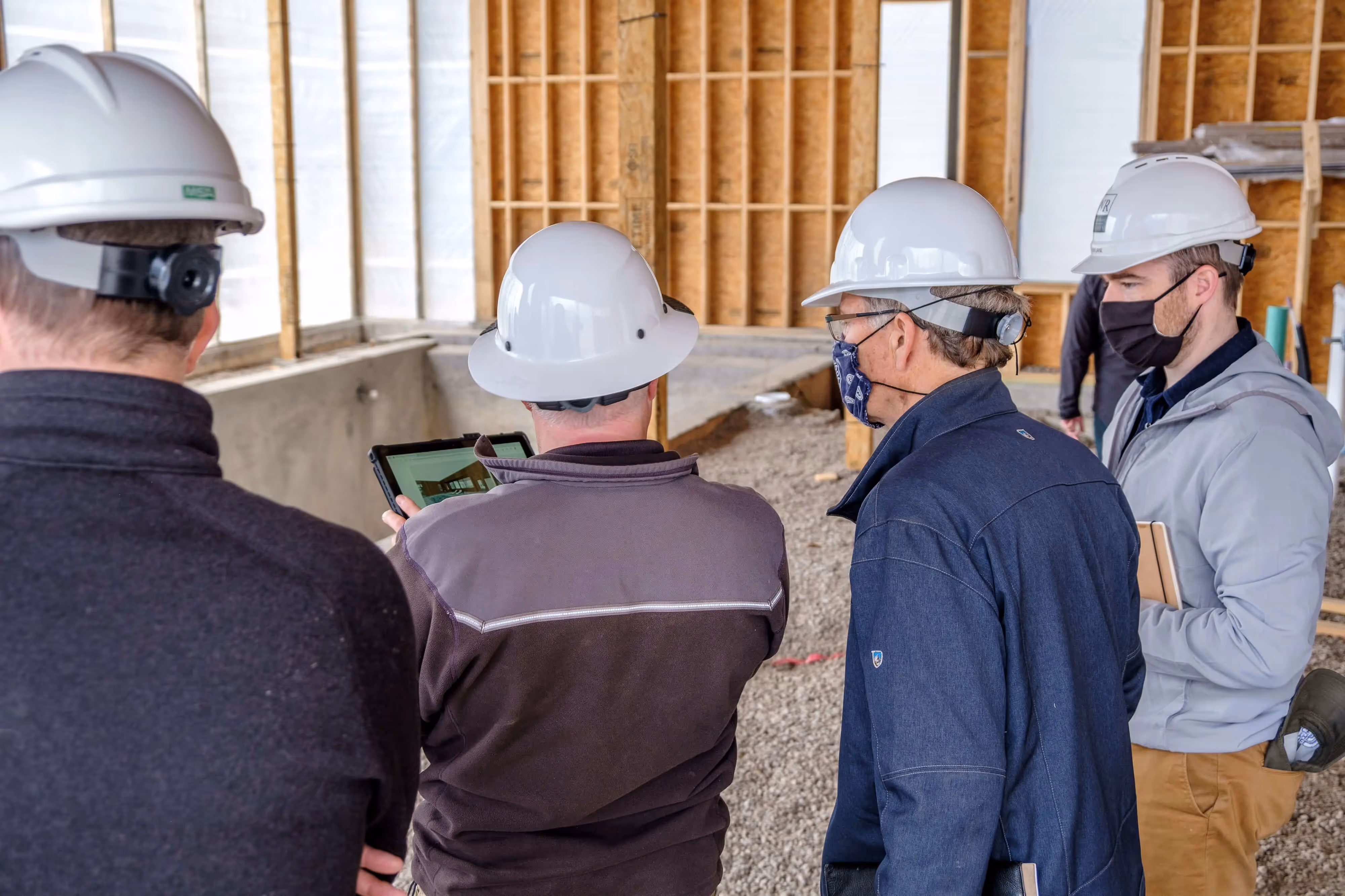 Construction workers in hard hats reviewing plans on a tablet at job site