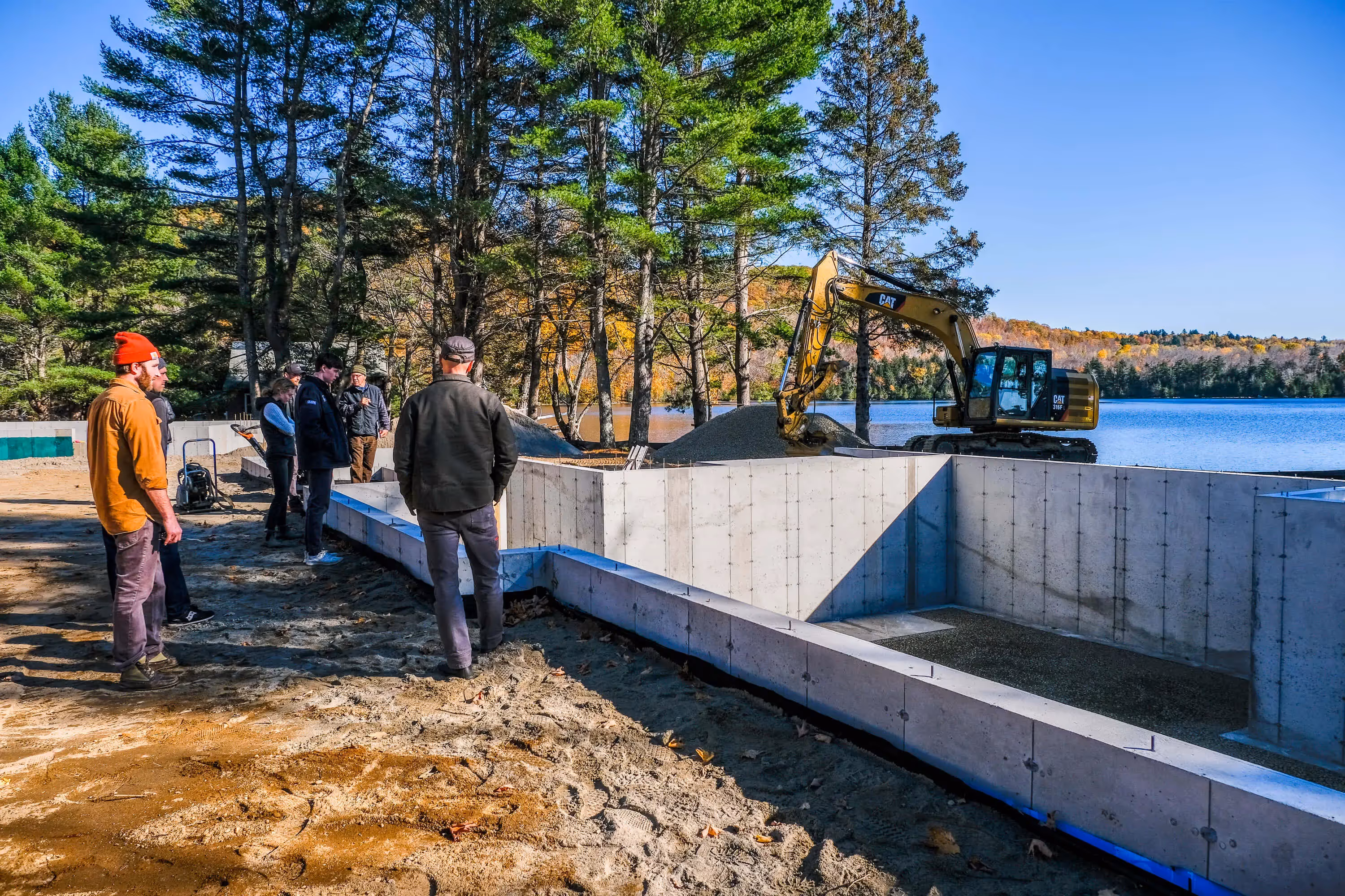 Construction site with excavator and workers near lake in autumn forest