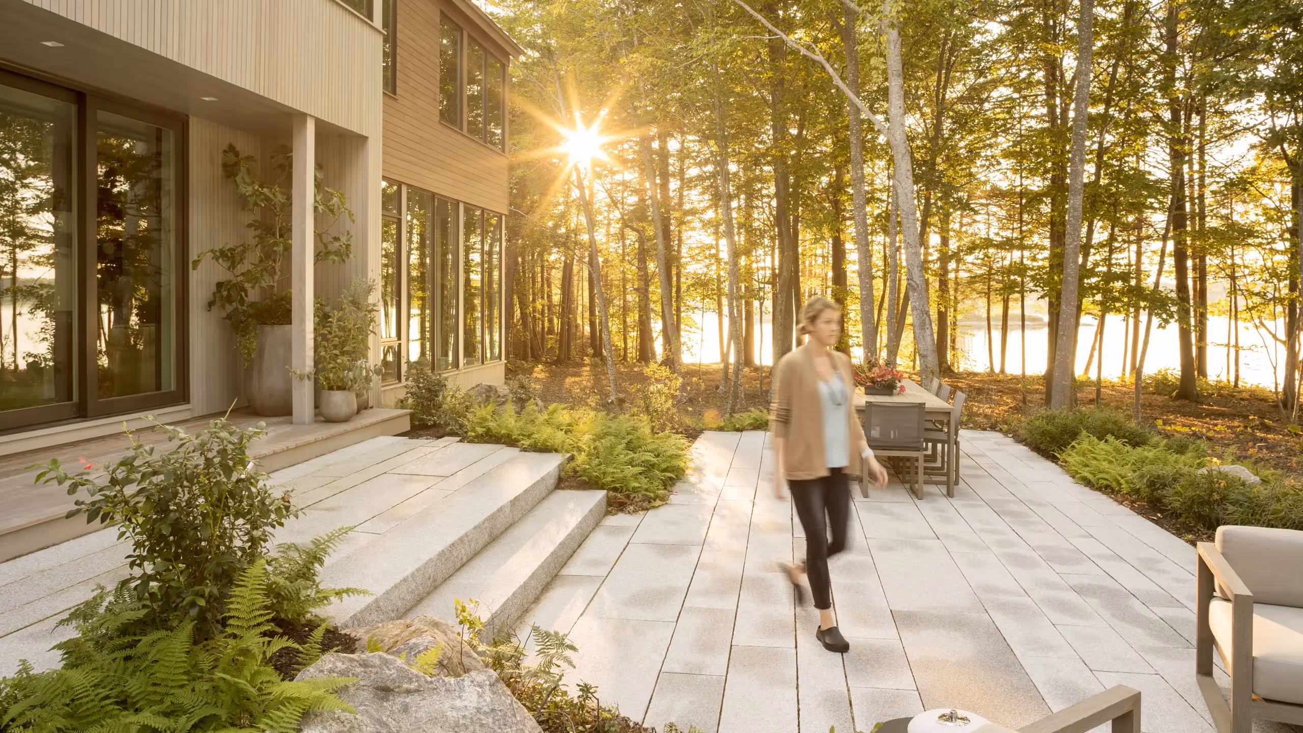 Sunlit patio with modern house, trees, and person walking on stone path