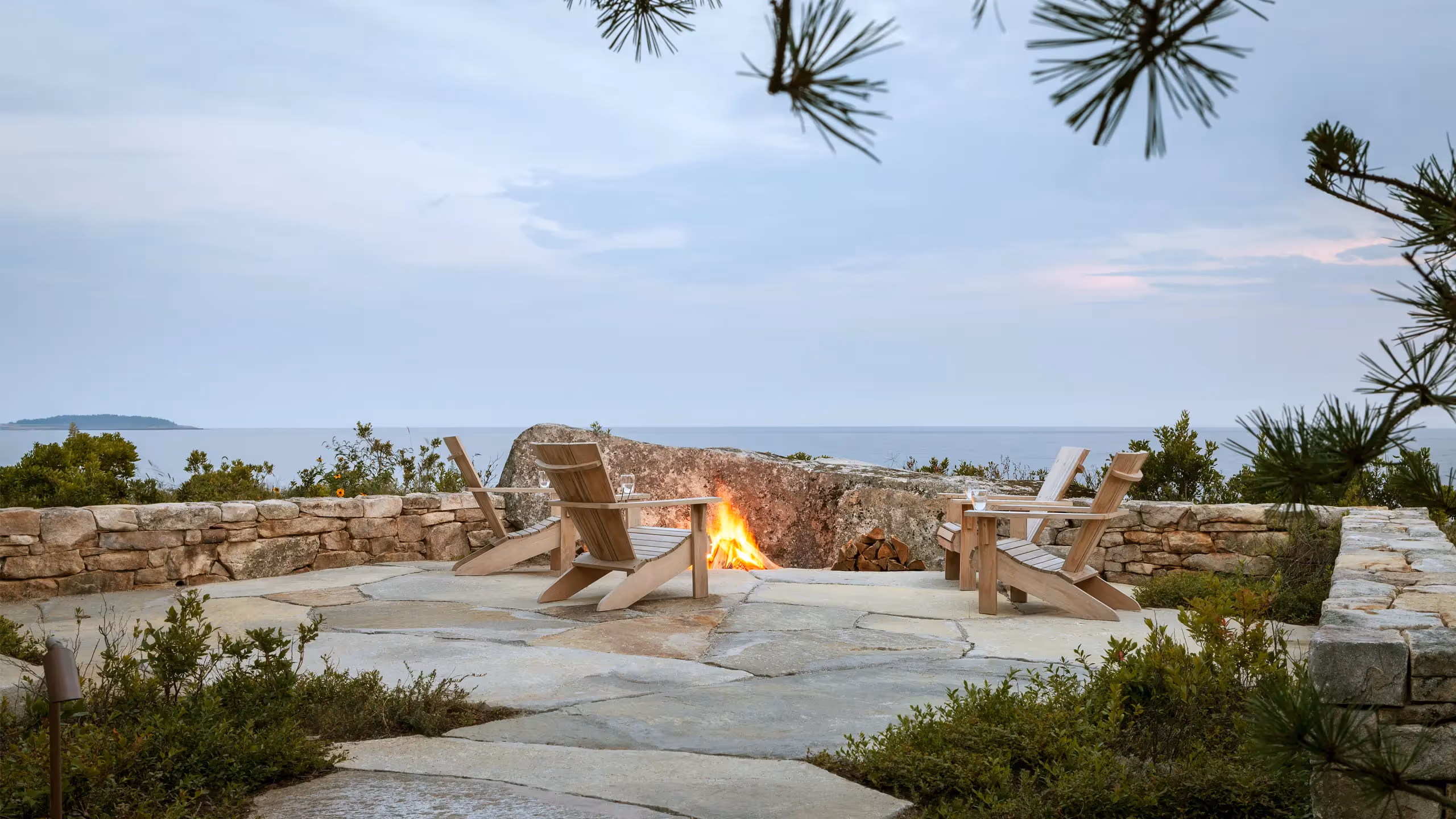 Cozy oceanside fire pit with Adirondack chairs and stone landscaping