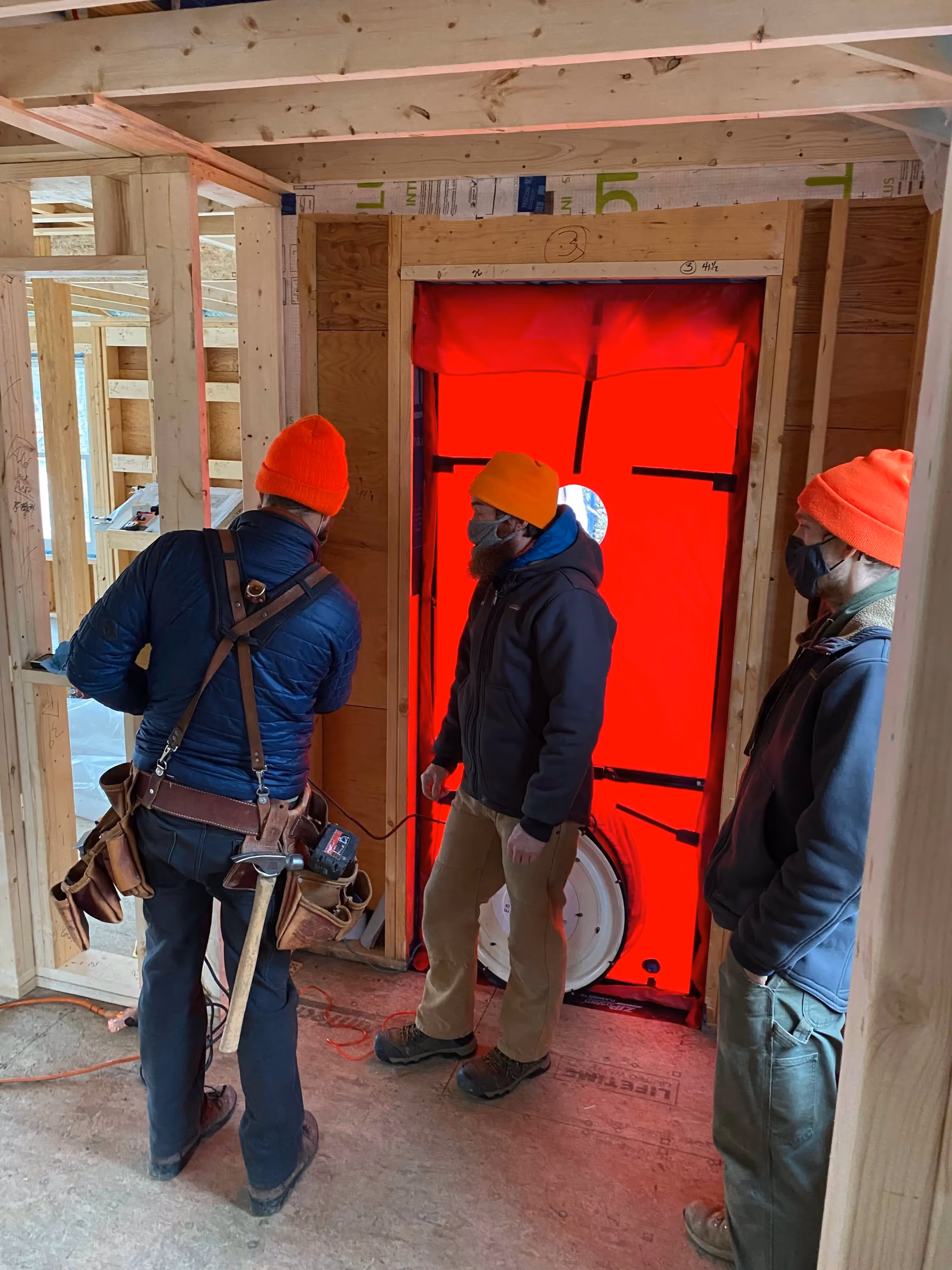 Construction workers examining bright red blower door during energy efficiency test