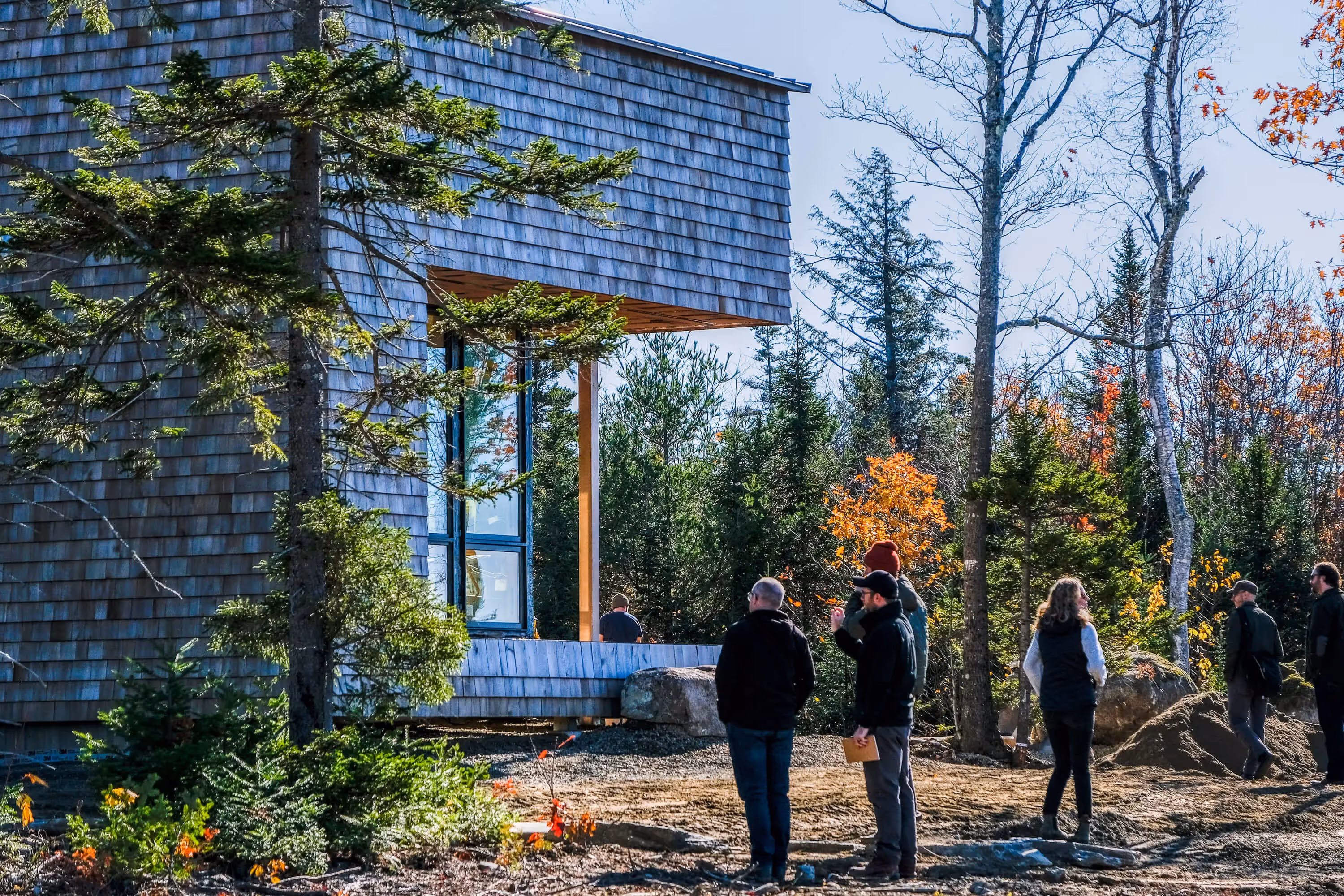 People exploring wooden building surrounded by trees in autumn landscape