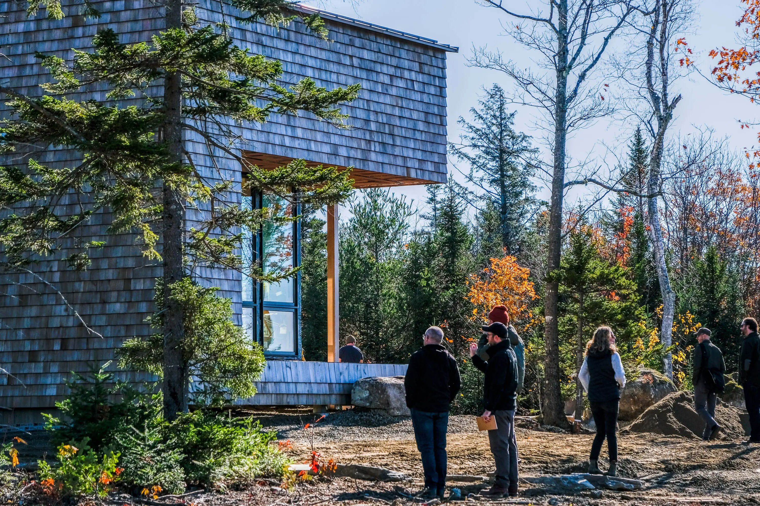 People exploring wooden building surrounded by trees in autumn landscape