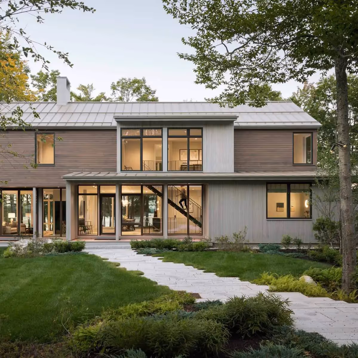 Modern two-story house with large windows surrounded by lush green landscape