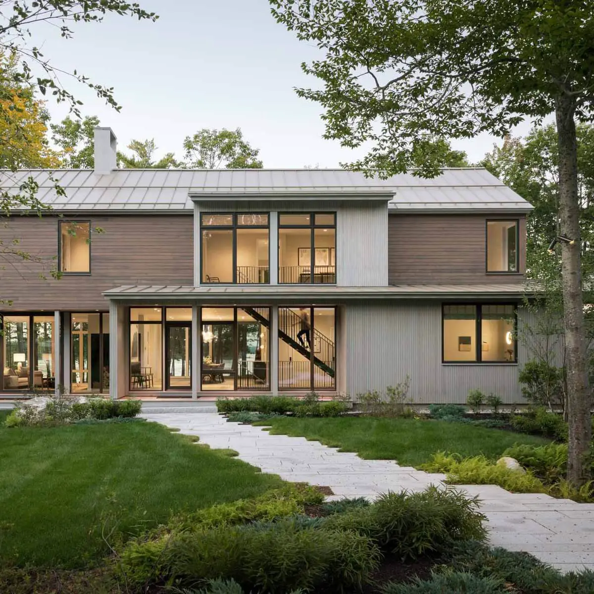 Modern two-story house with large windows surrounded by lush green landscape