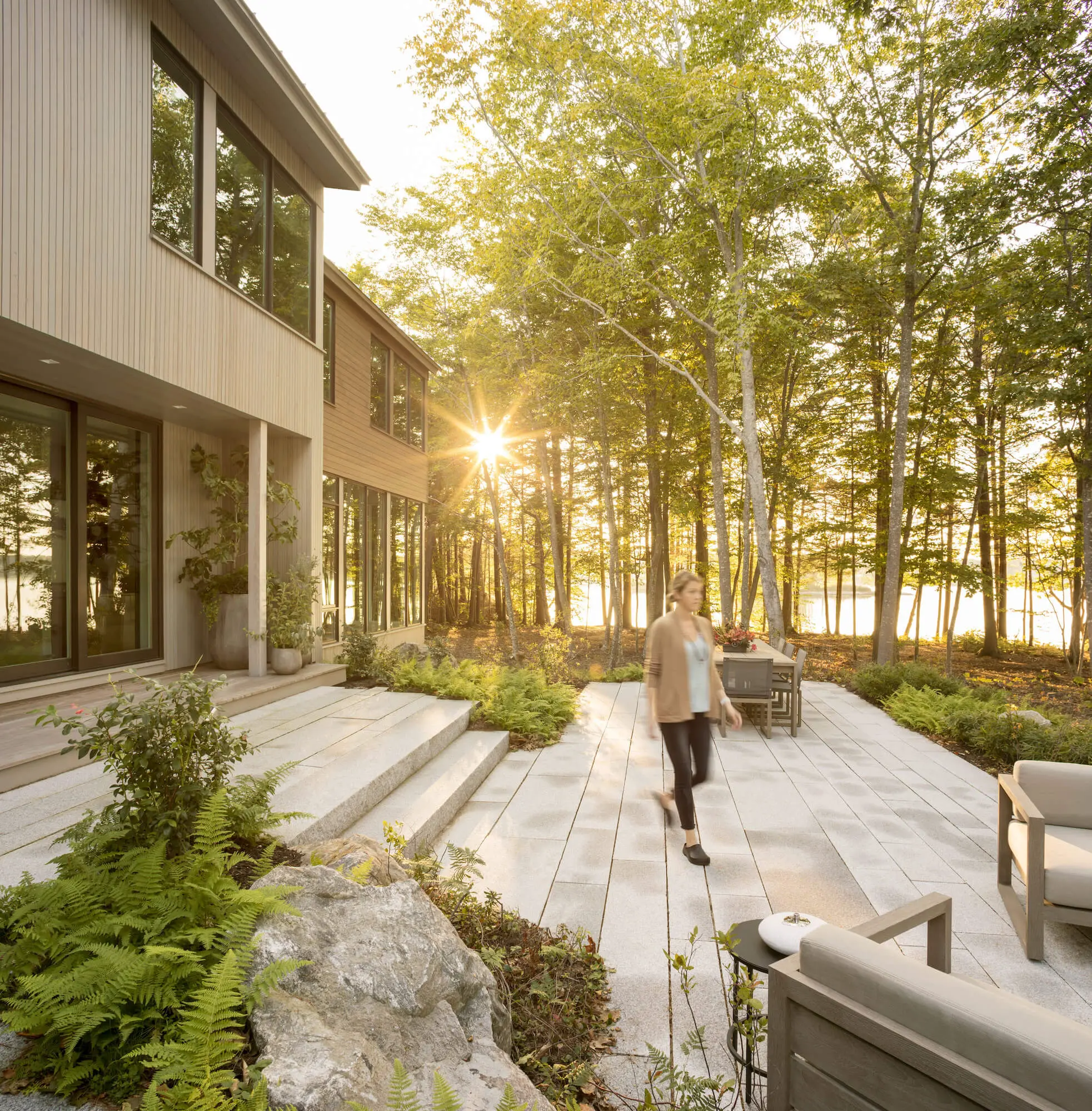Modern home patio with sunlight filtering through trees near water