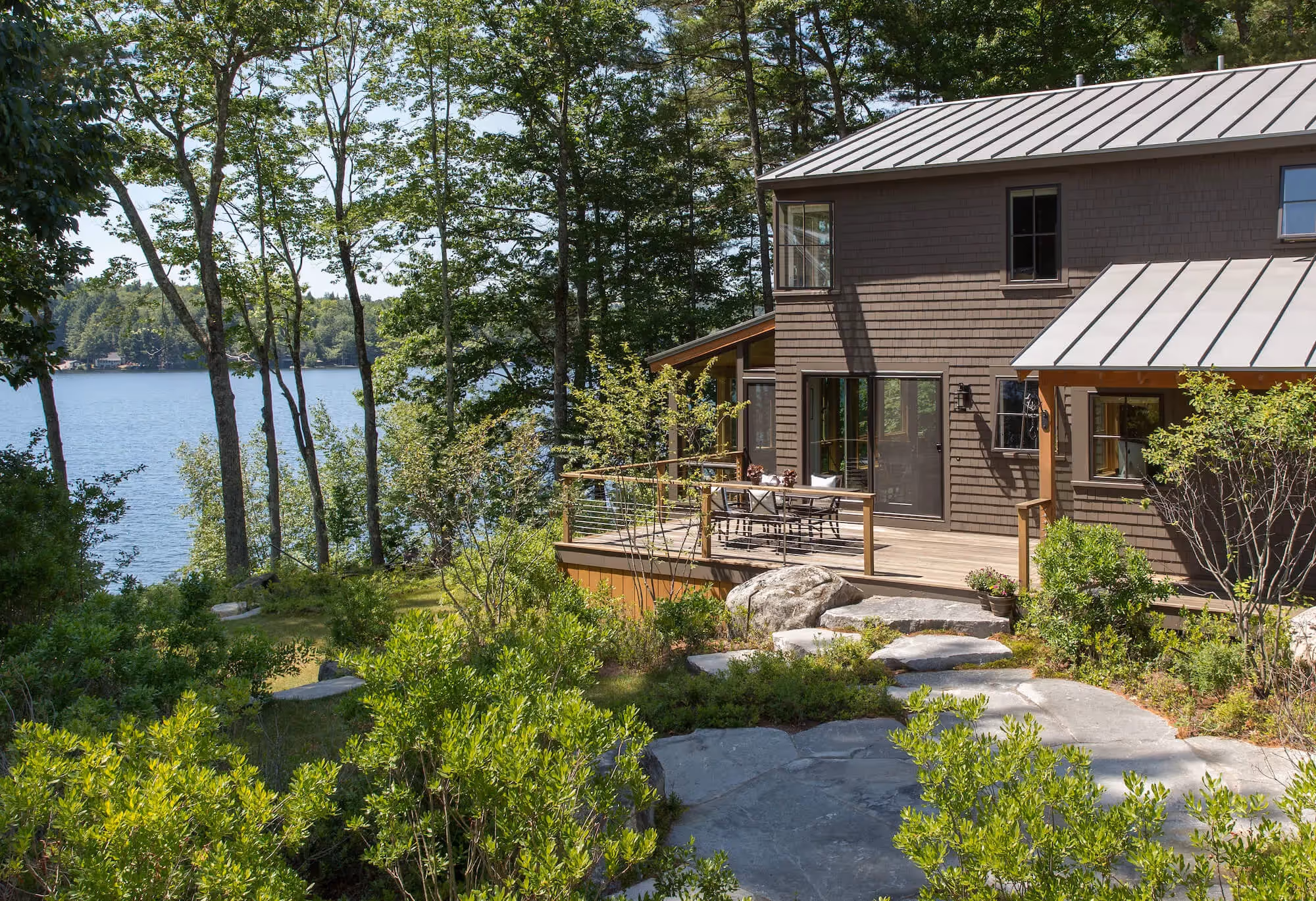Lakeside wooden house with deck, surrounded by trees and stone path