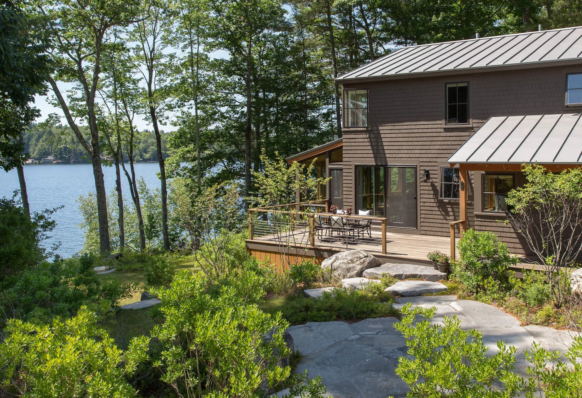 Lakeside wooden house with deck, surrounded by trees and stone path