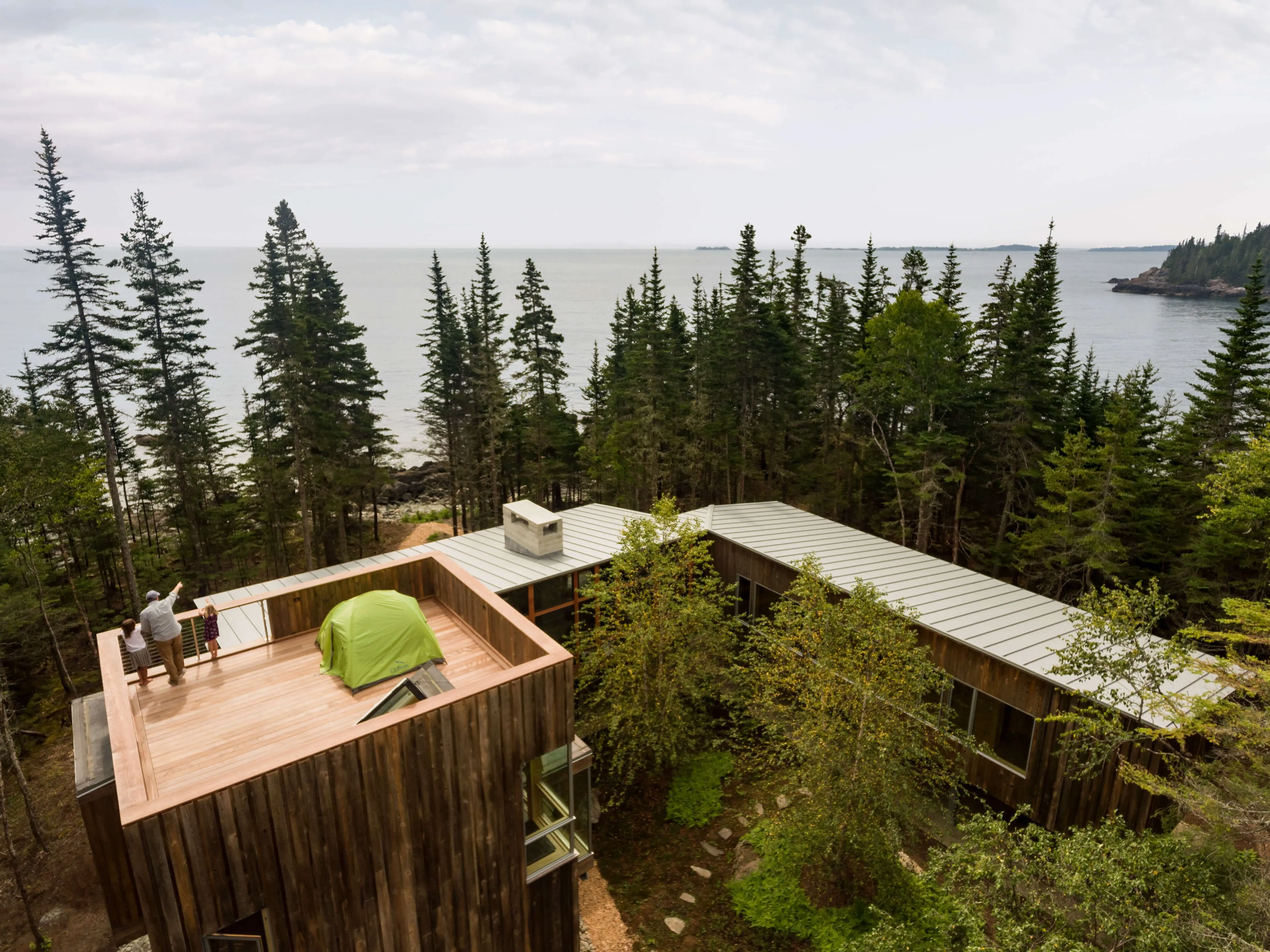Wooden cabin with green tent on roof overlooking forested coastal landscape