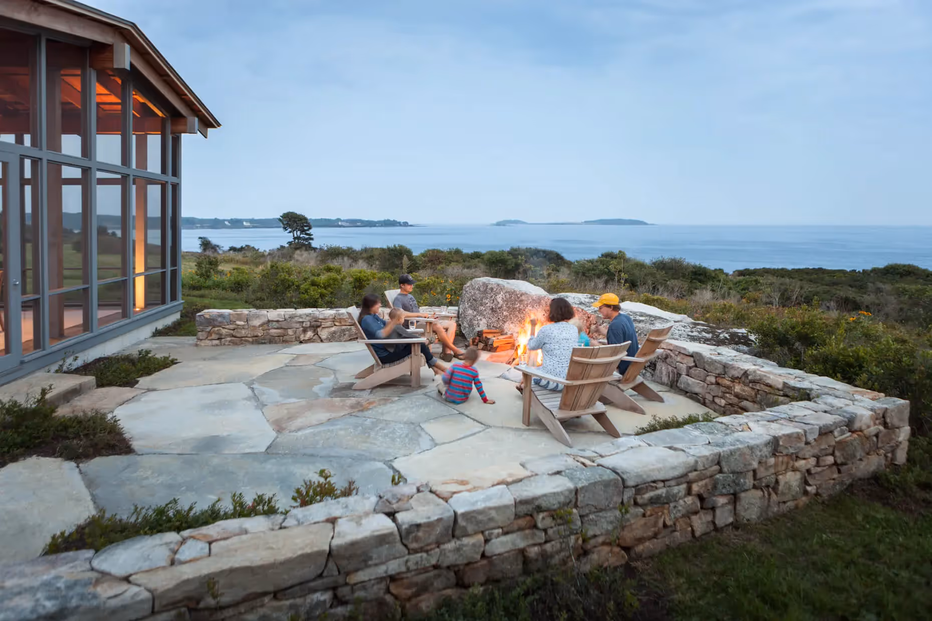 Family gathering around fire pit with ocean view at coastal stone patio