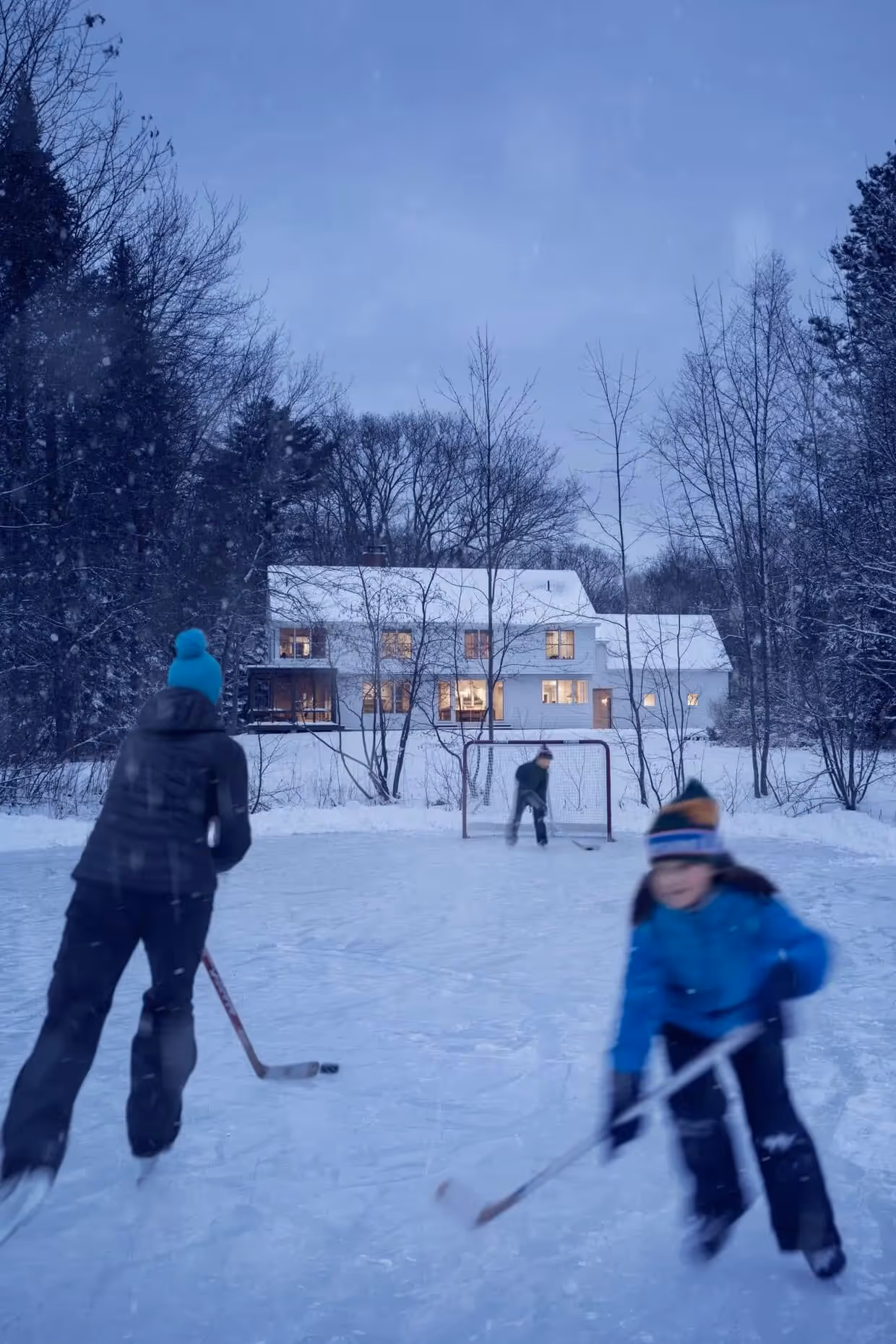 Outdoor hockey game on snowy backyard rink near cozy winter house