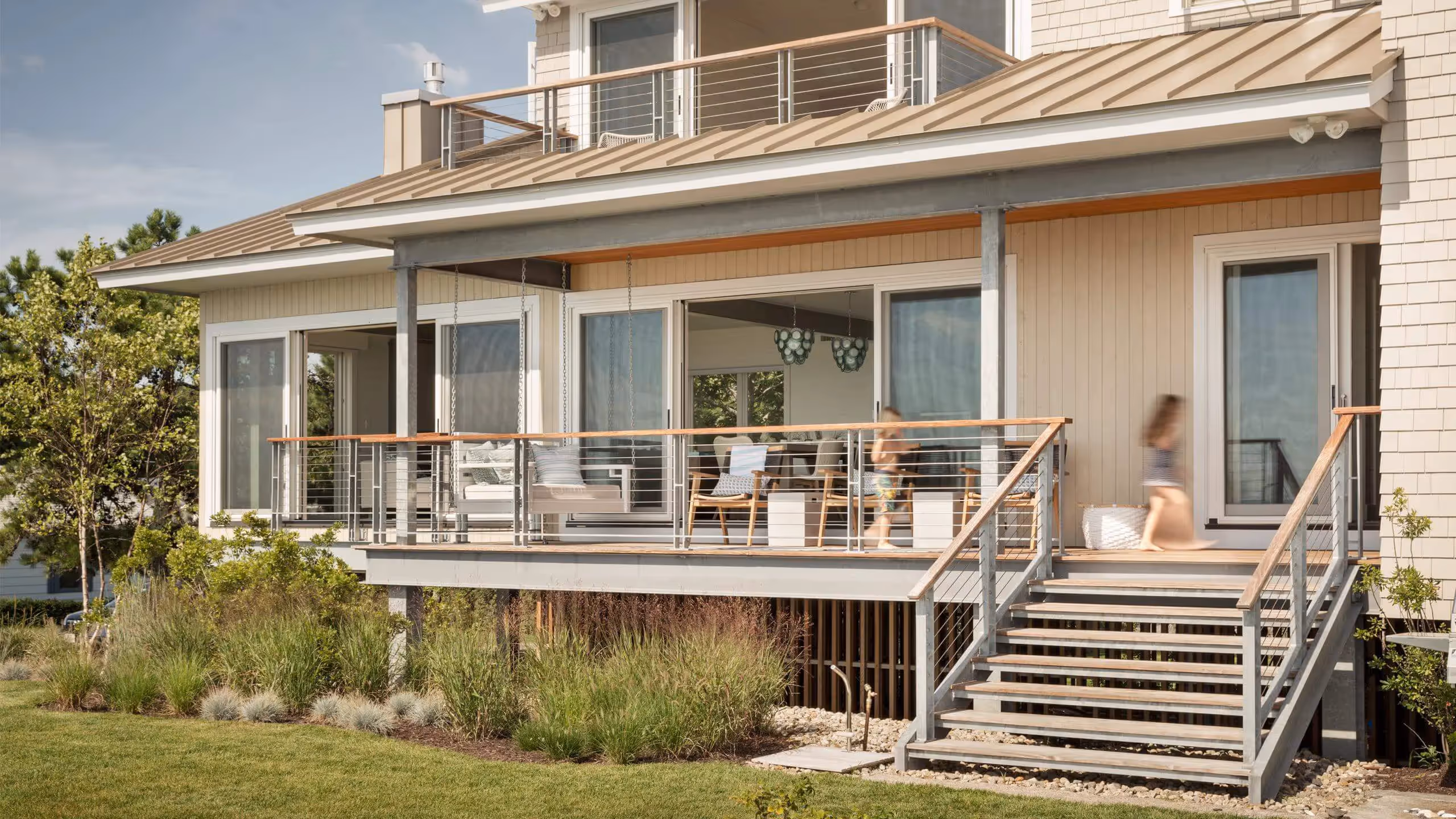 Modern beach house with large deck, metal railings, and landscaped surroundings