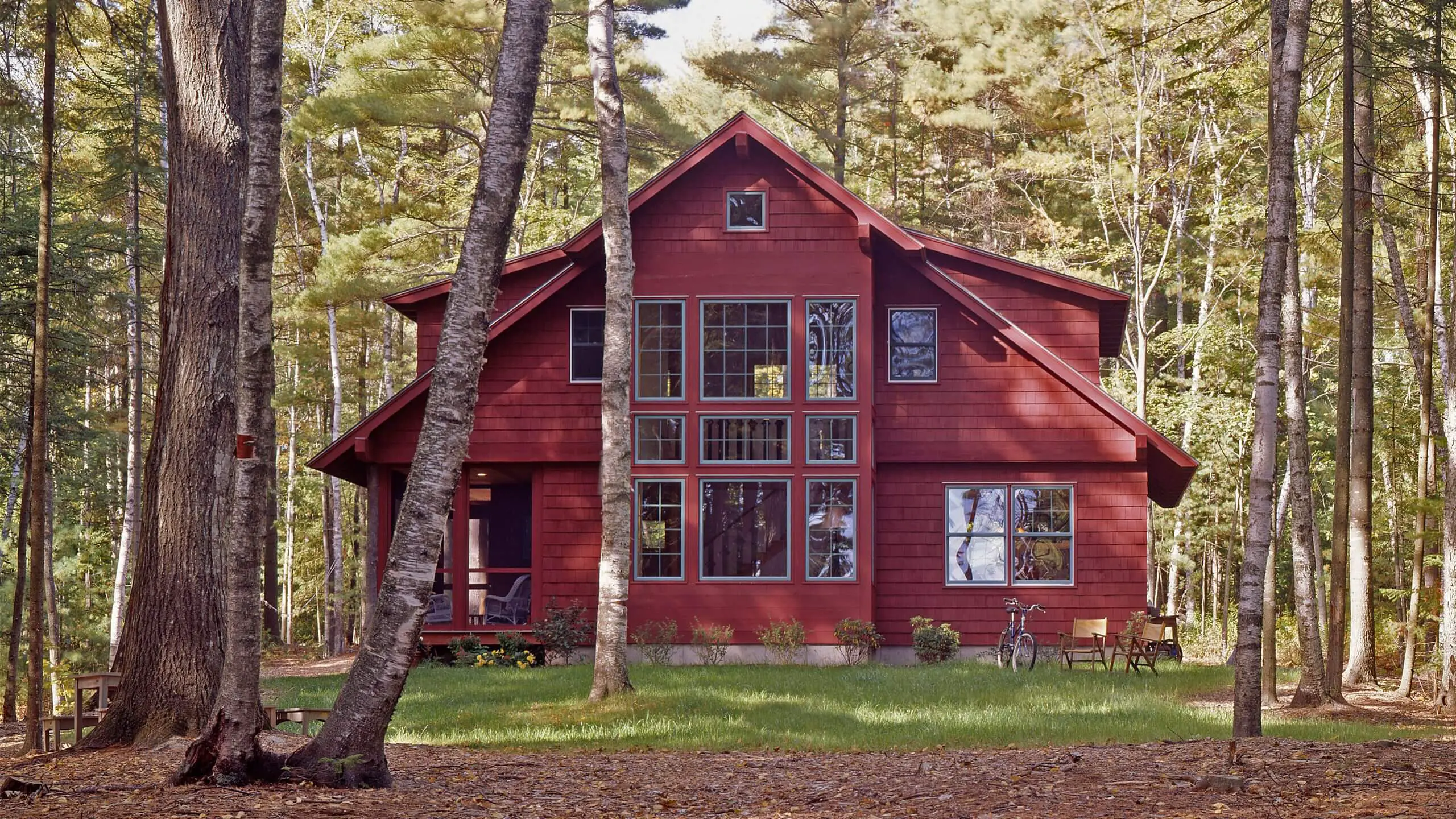 Red wooden cabin nestled in a peaceful forest with trees surrounding it