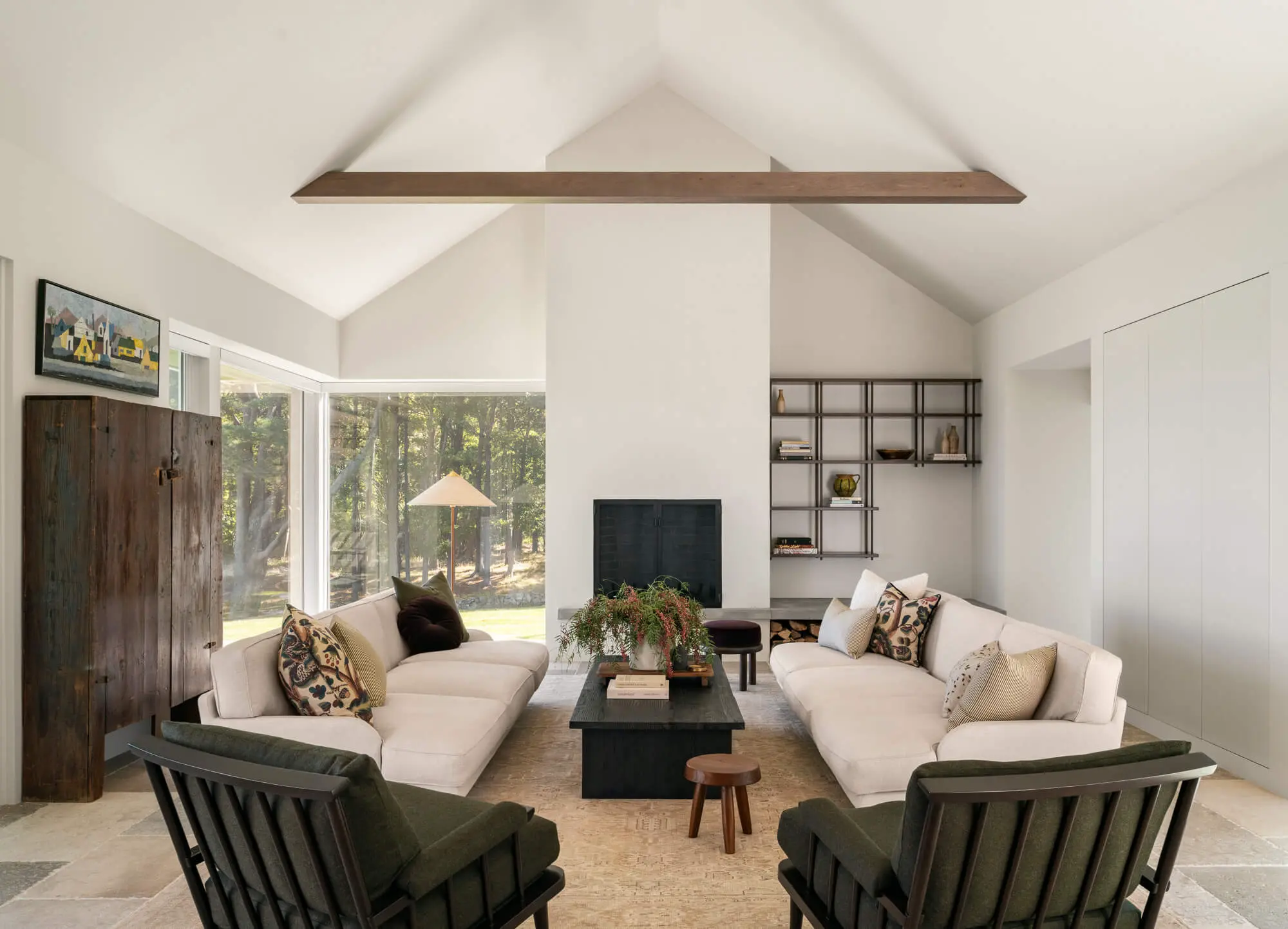 Modern living room with white sofas, fireplace, and forest view windows