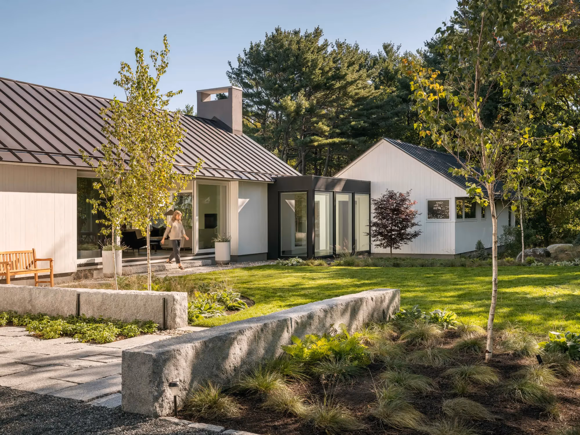 Modern white house with metal roof, stone walls, and lush green landscaping