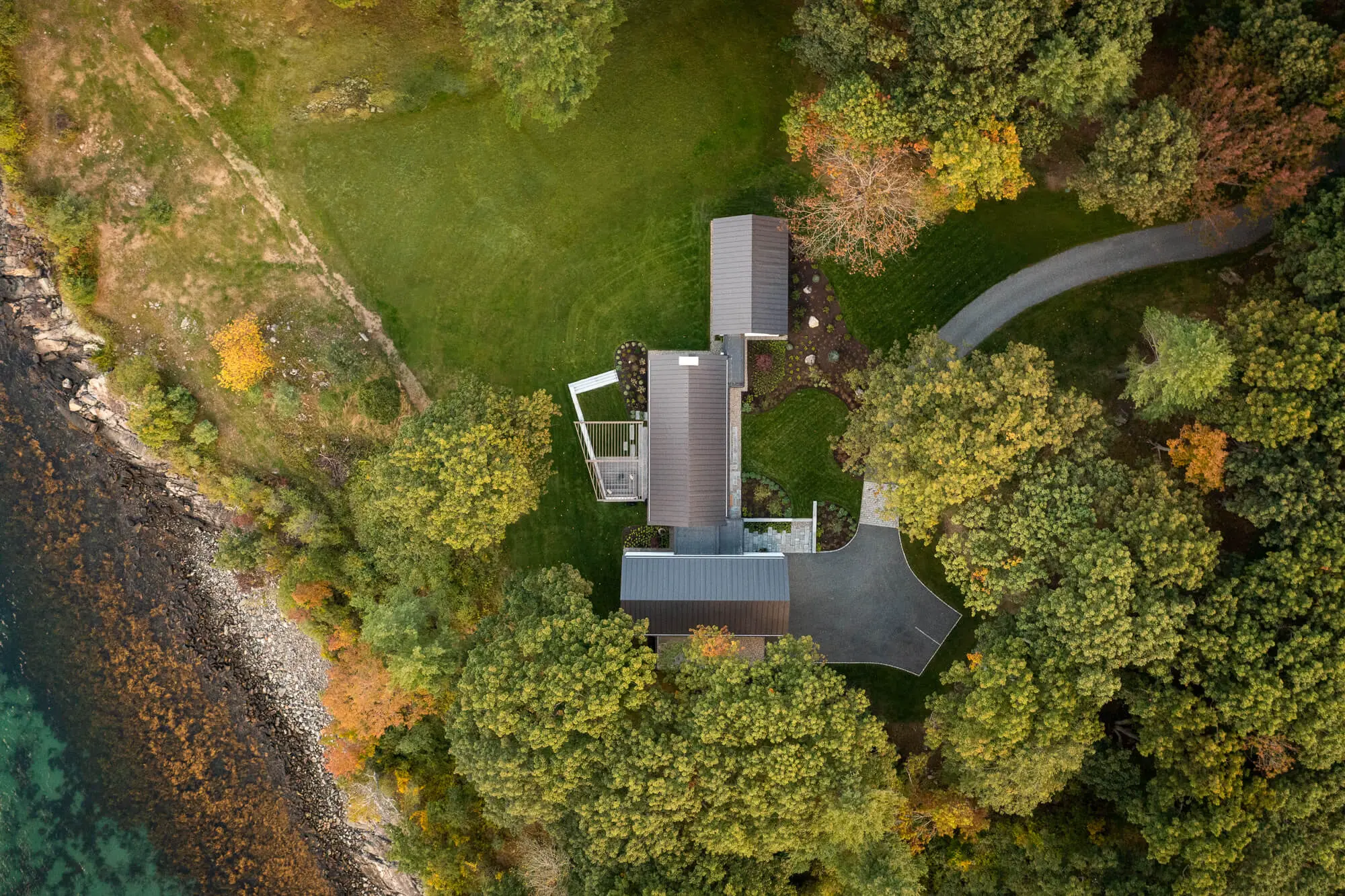 Modern house nestled in forest with winding road and autumn trees