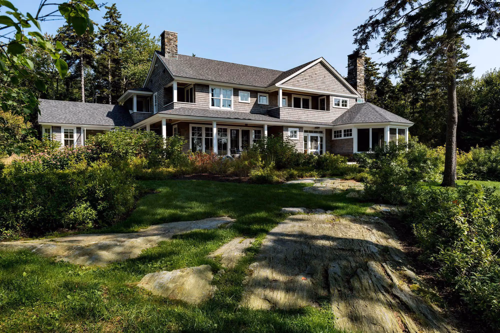 Shingle-style house with stone accents nestled in lush green landscaping