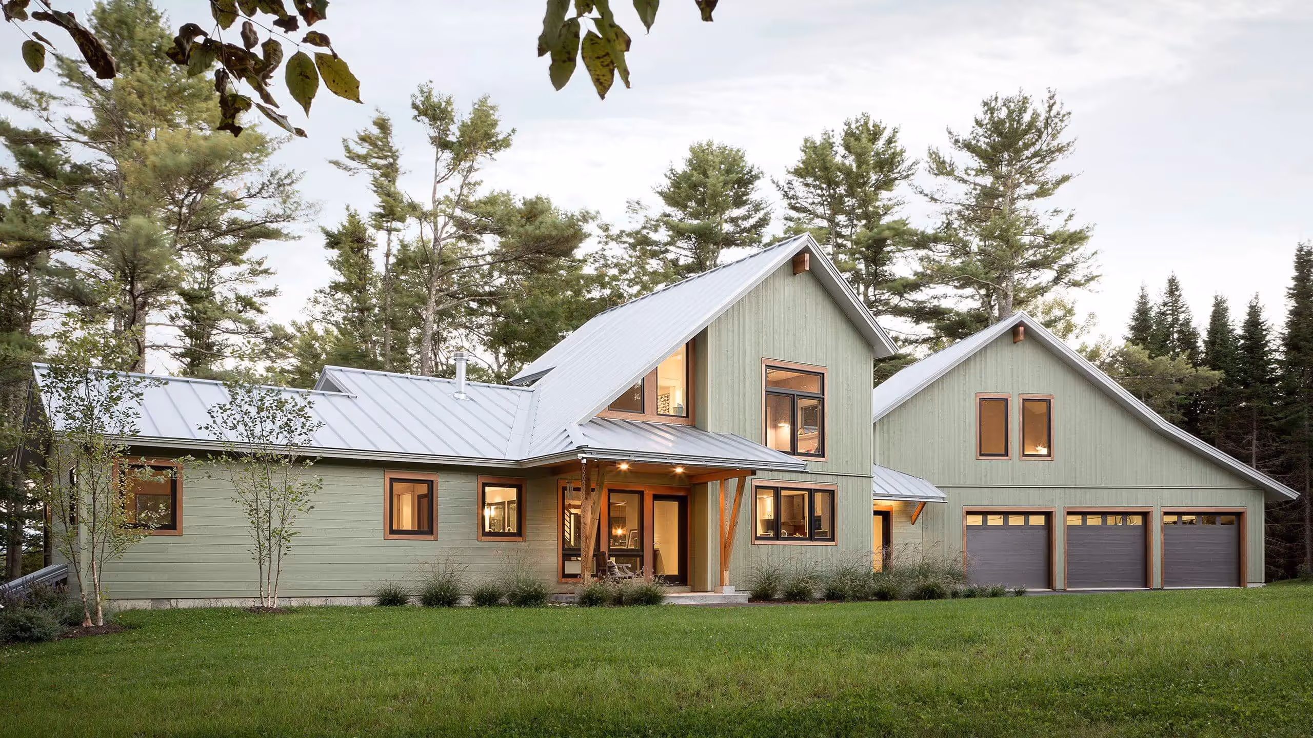 Modern green farmhouse with metal roof nestled among pine trees