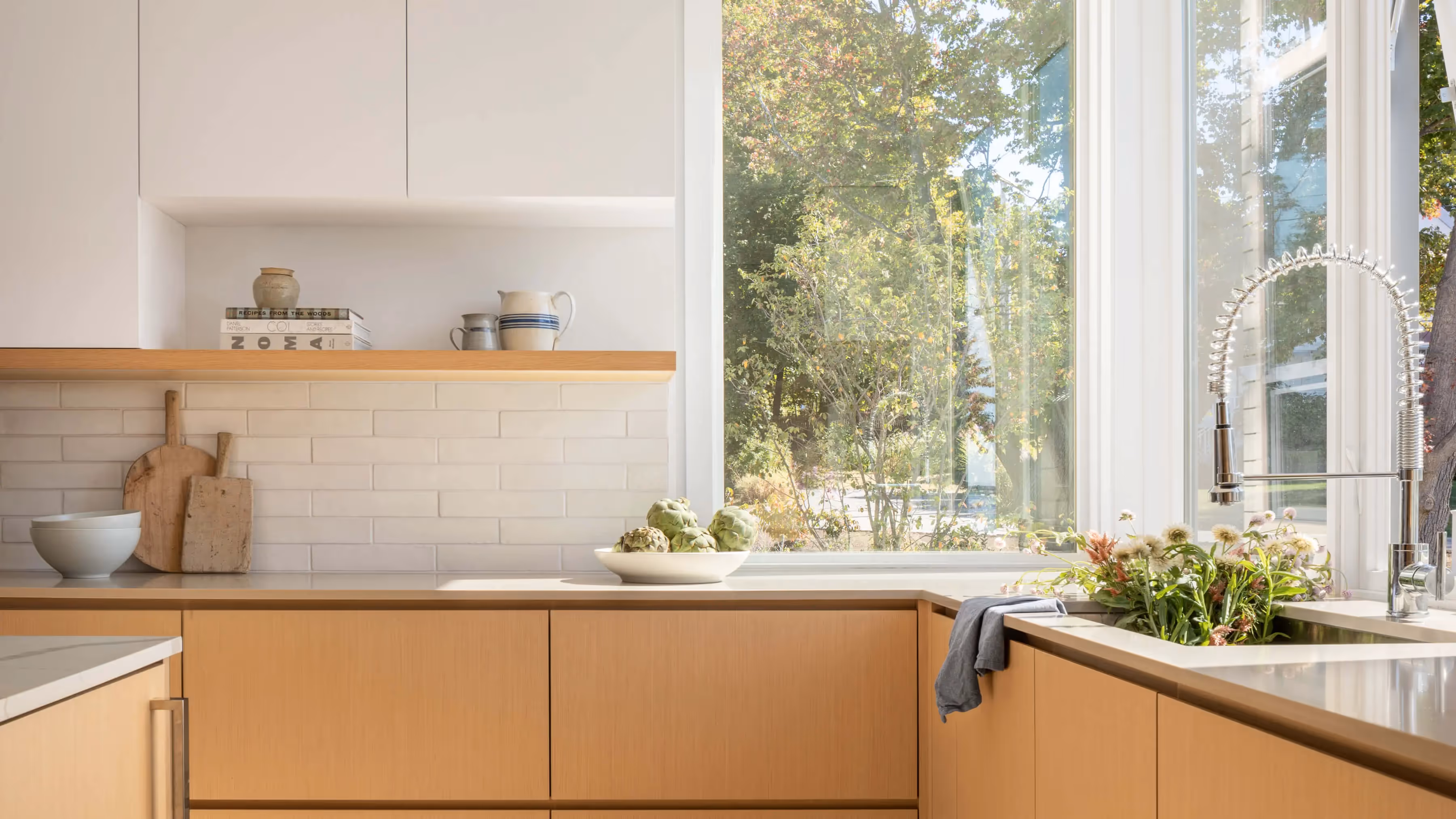 Modern kitchen with wooden cabinets, white tiles, and large windows overlooking trees