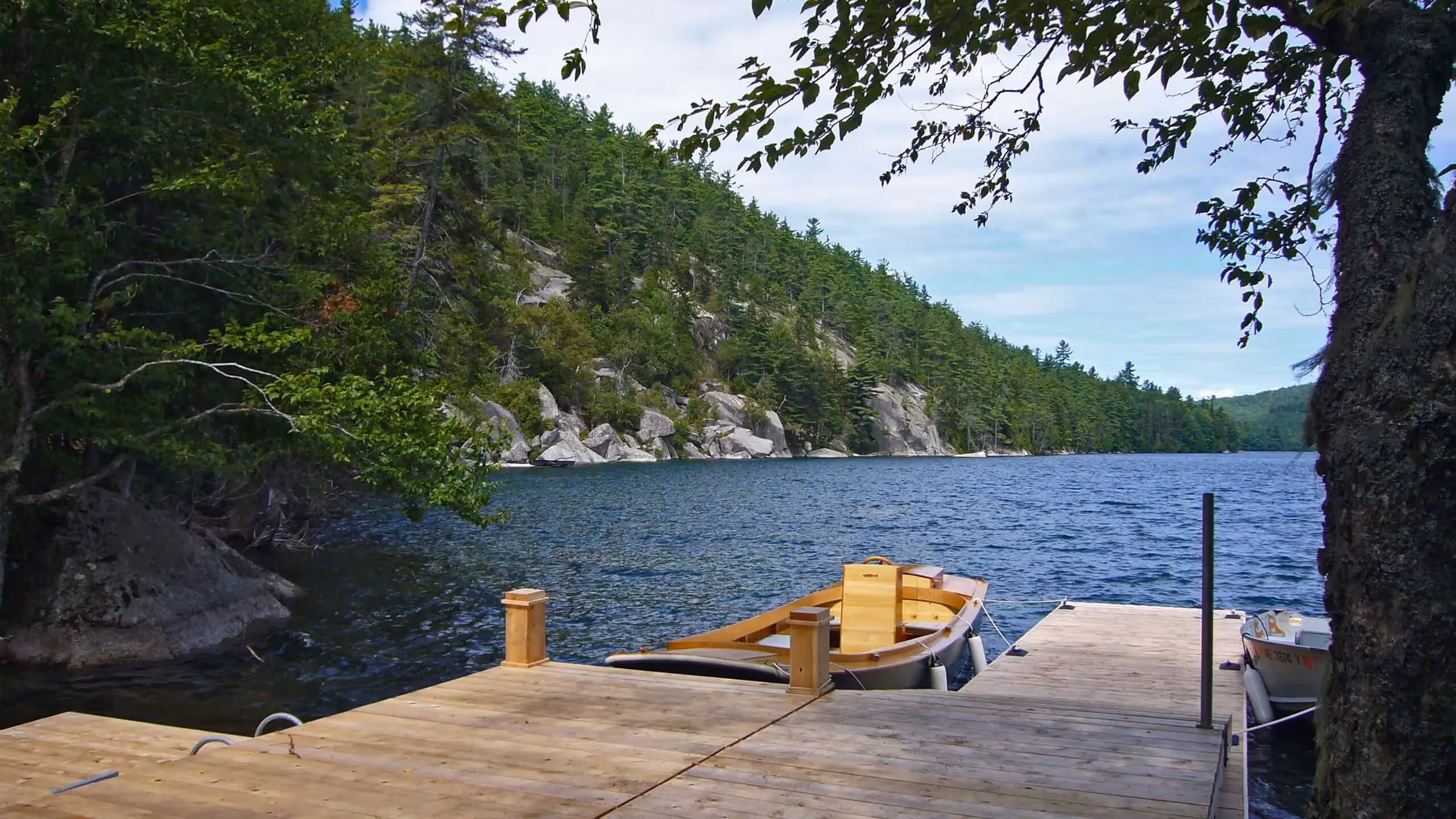 Yellow boat docked on wooden pier by rocky lake surrounded by pine forest