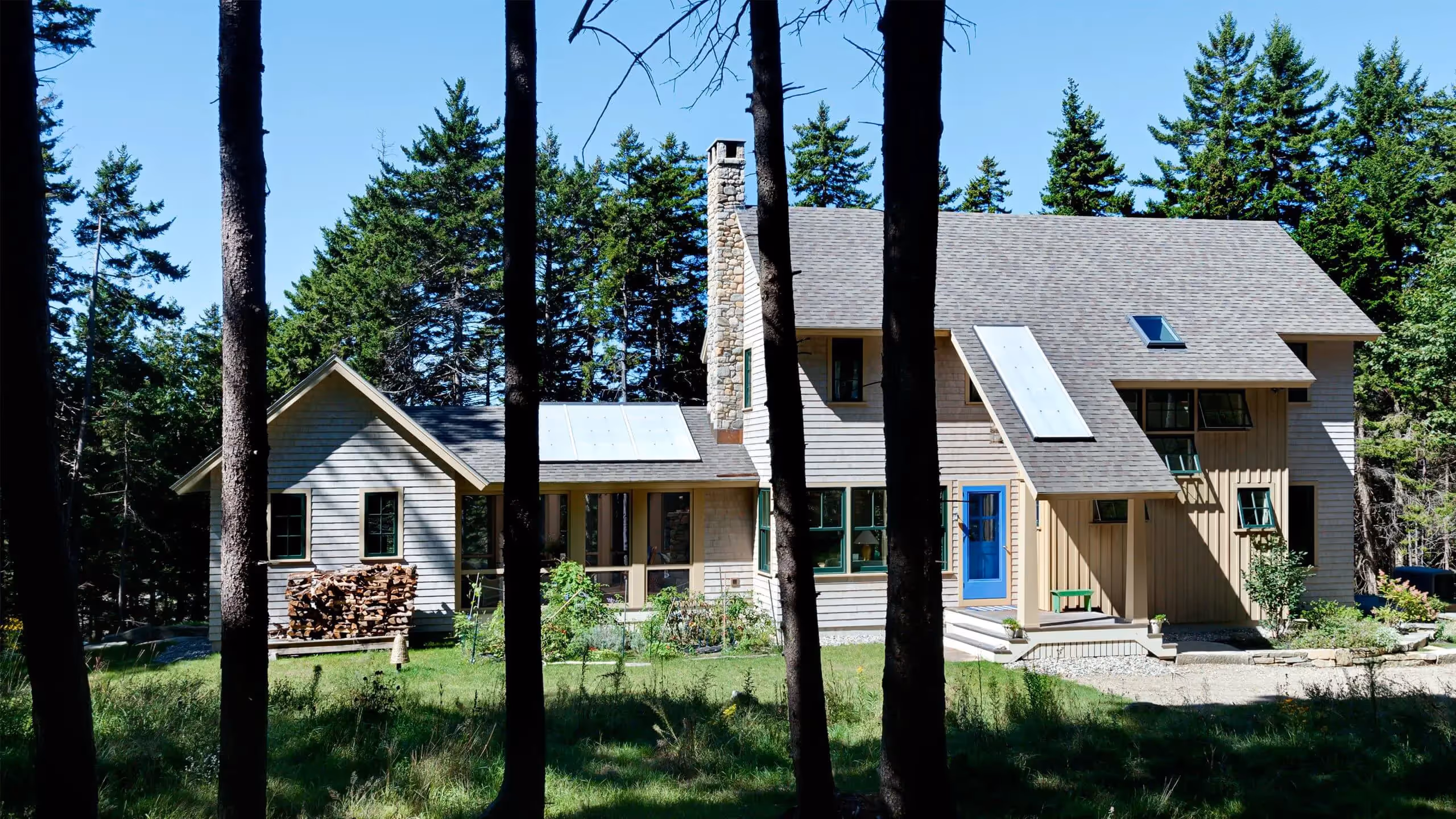 Wooden houses with blue door in sunny forest clearing with firewood stack