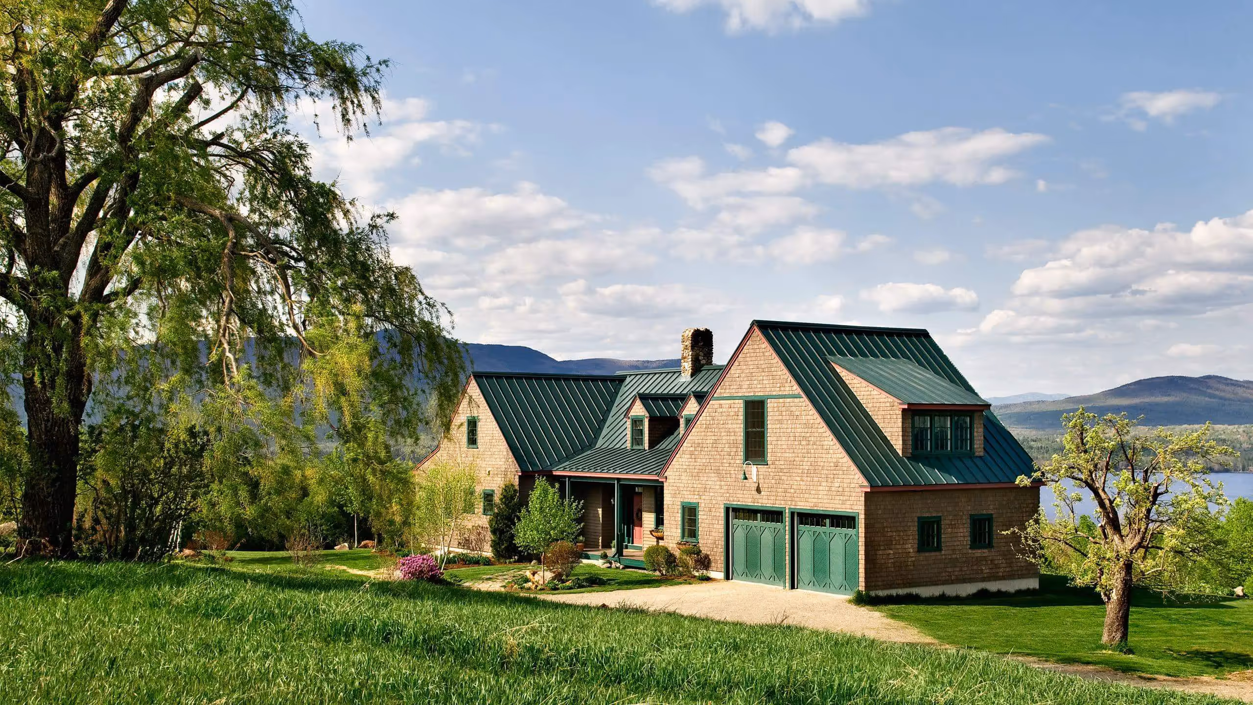 Rustic house with green metal roof nestled in lush landscape with mountains and lake