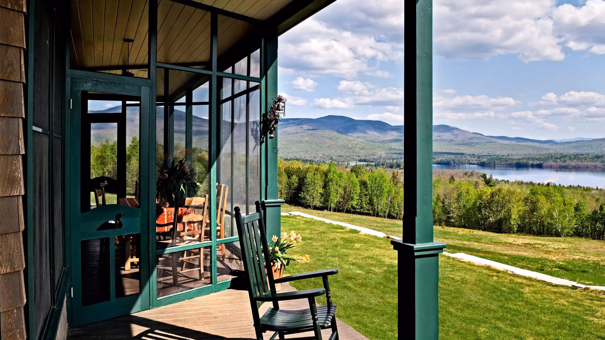 Serene mountain view from porch with green rocking chair and lake