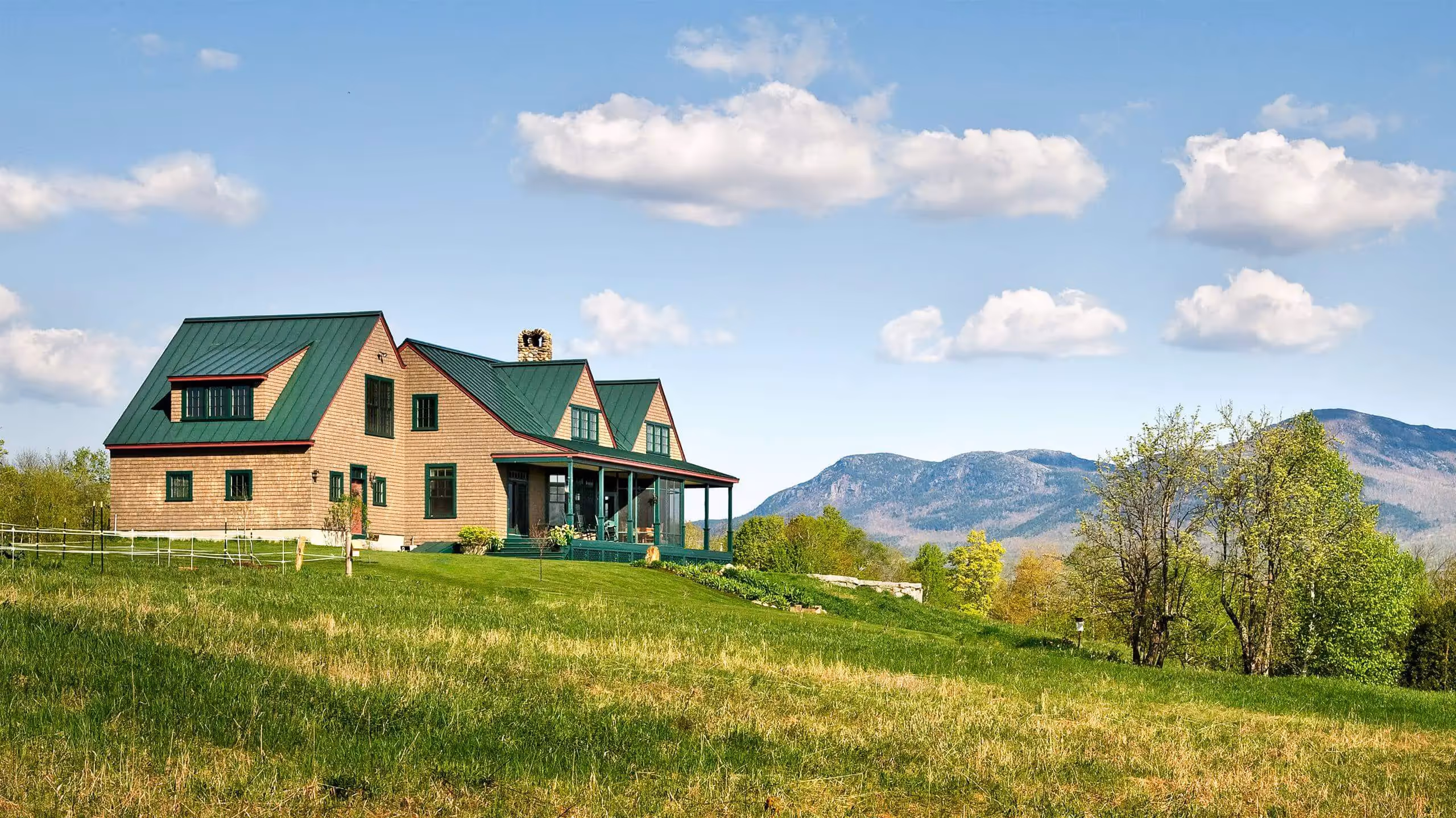 Wooden house with green roof on grassy hill with mountain landscape