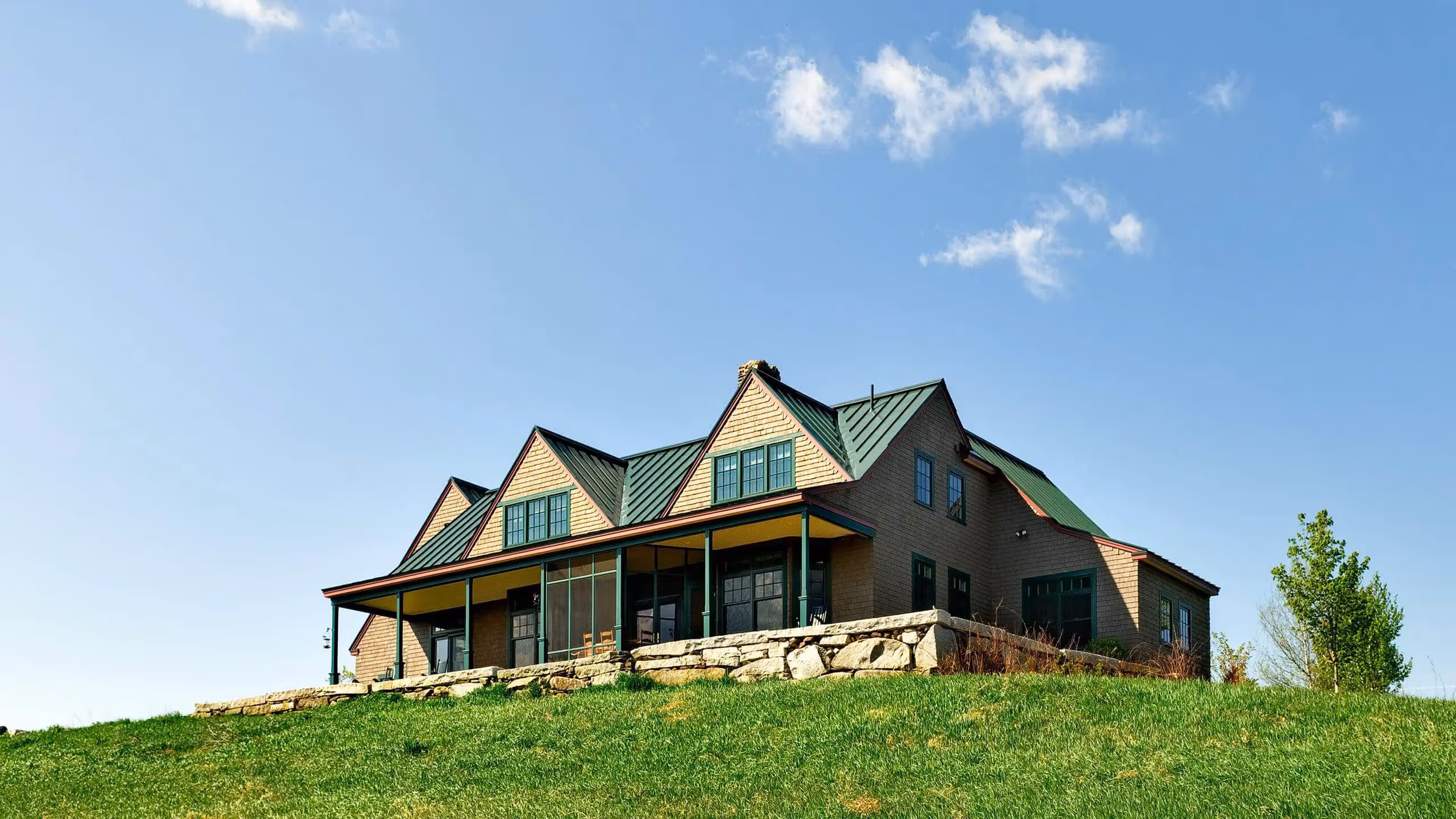Modern farmhouse with green roof on grassy hill under blue sky