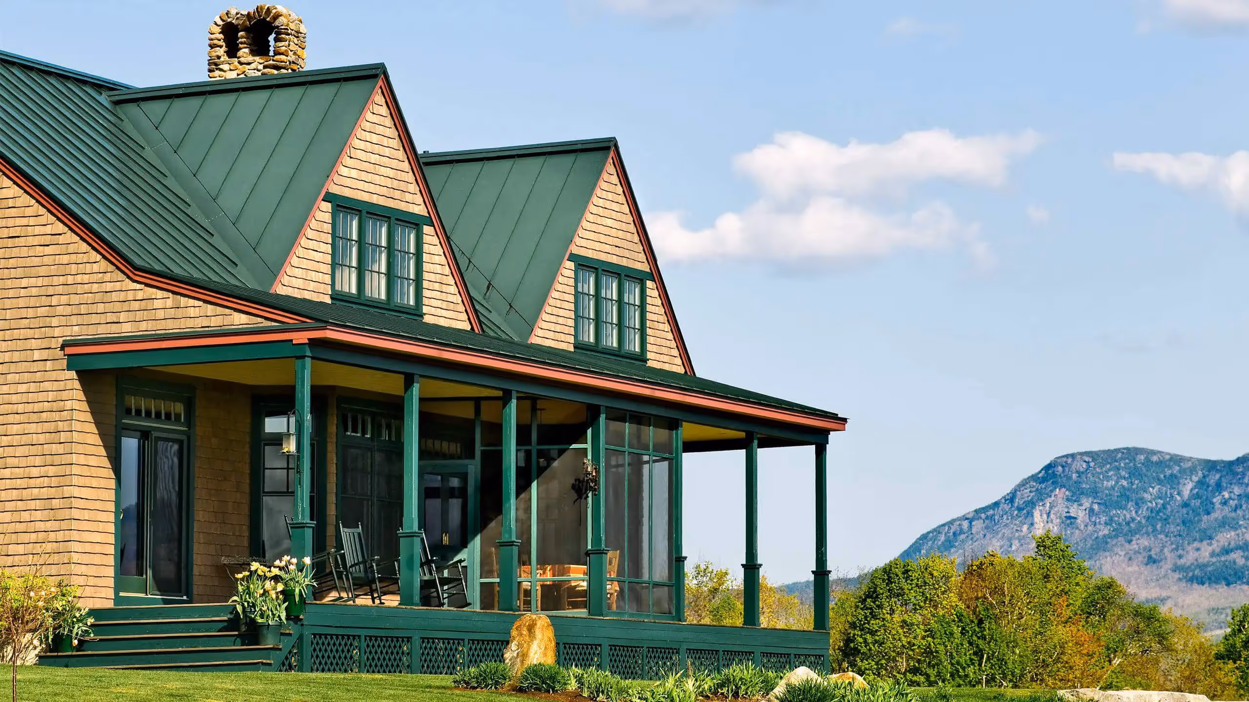 Green-roofed cottage with porch overlooking mountain landscape