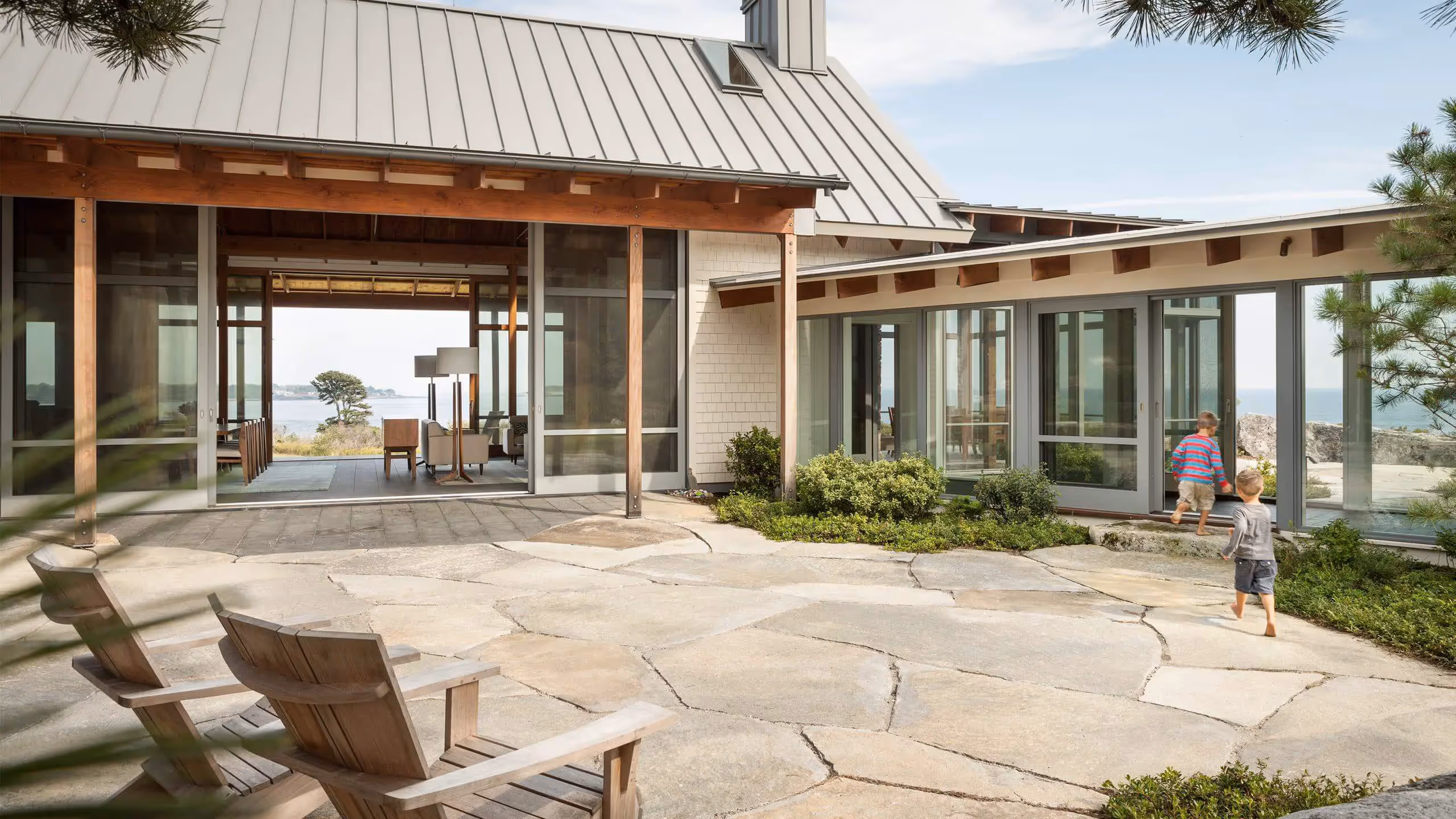 Modern beach house with stone patio, wooden chairs, and ocean view