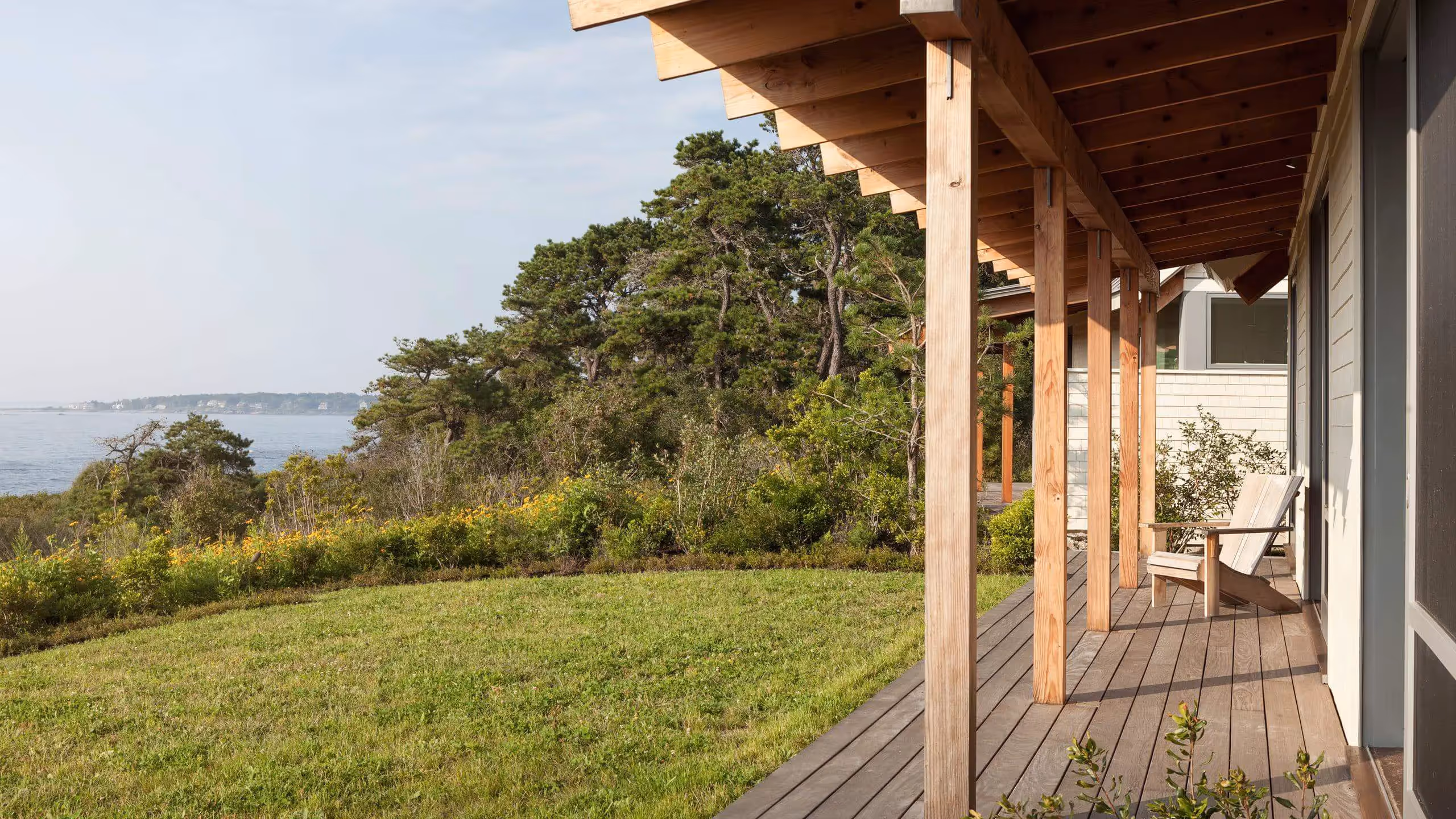 Wooden deck overlooking grassy yard and ocean with pine trees