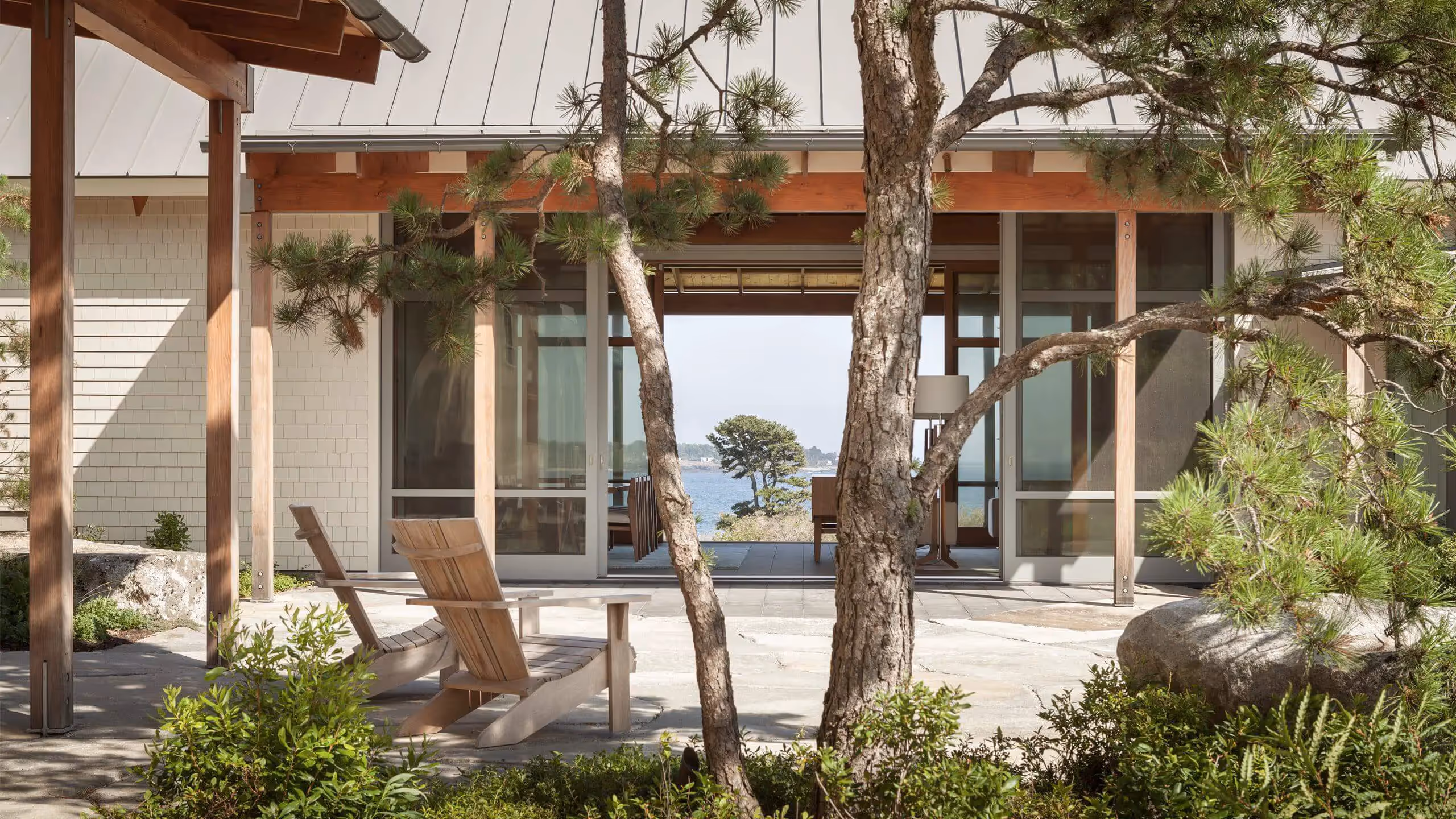 Coastal wooden house with pine trees and Adirondack chair overlooking ocean