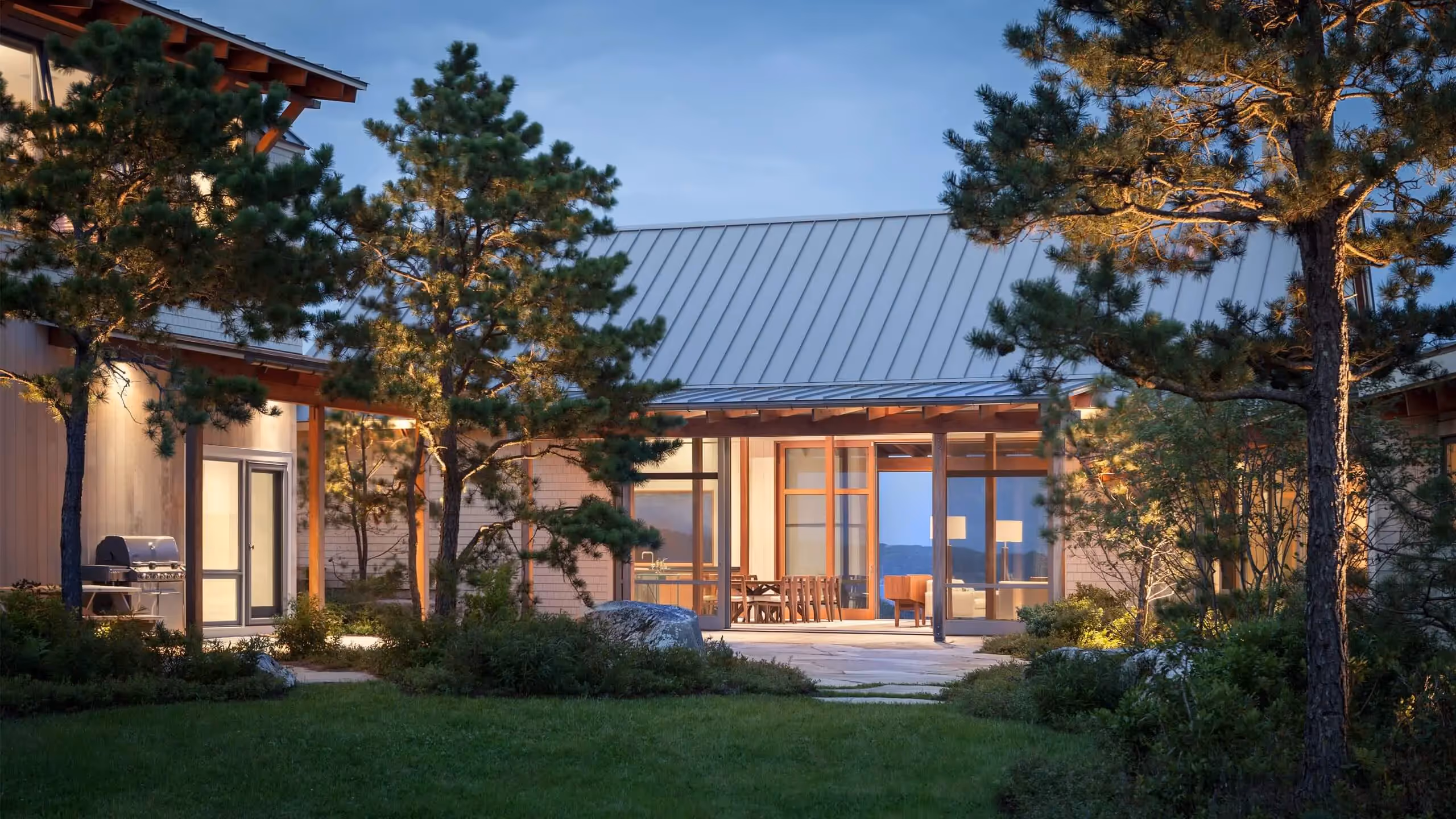 Modern house with large windows surrounded by pine trees at dusk