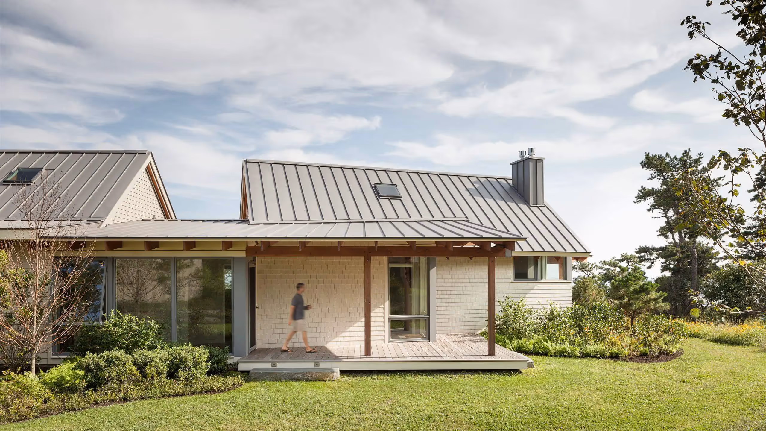 Modern house with metal roof and wooden deck surrounded by green landscape