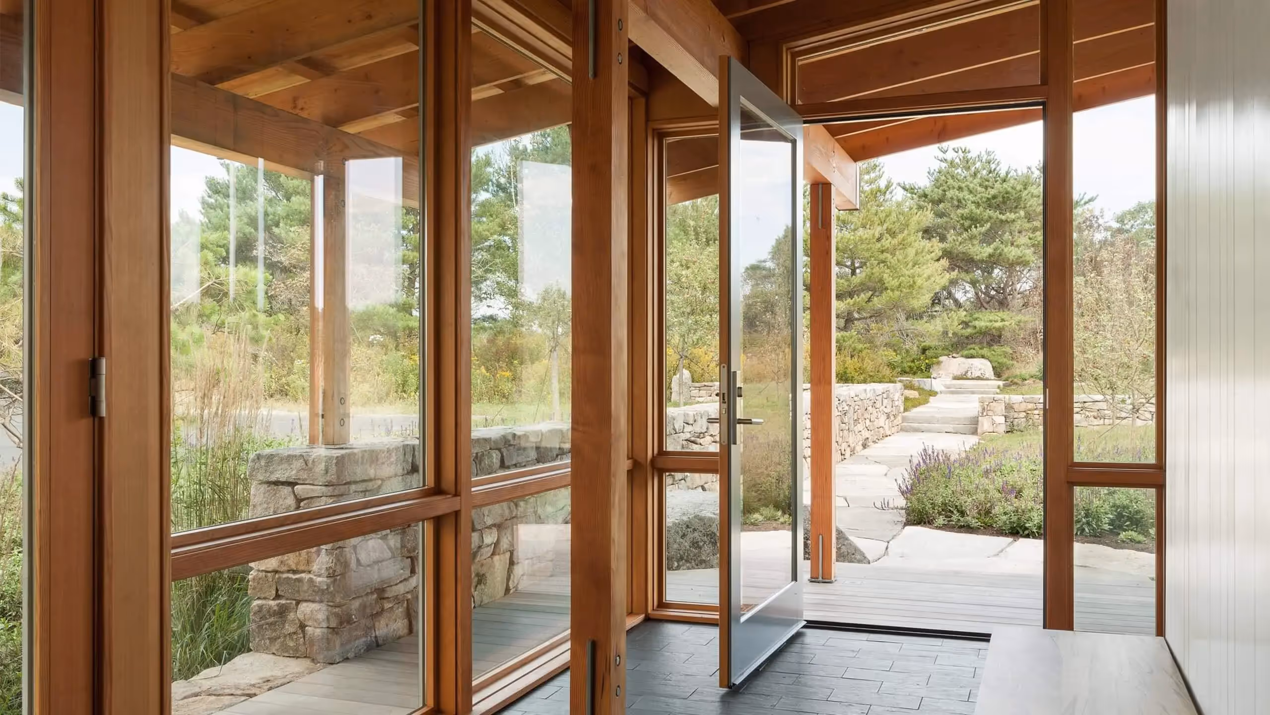 Wooden glass doors open to stone path and lush garden landscape