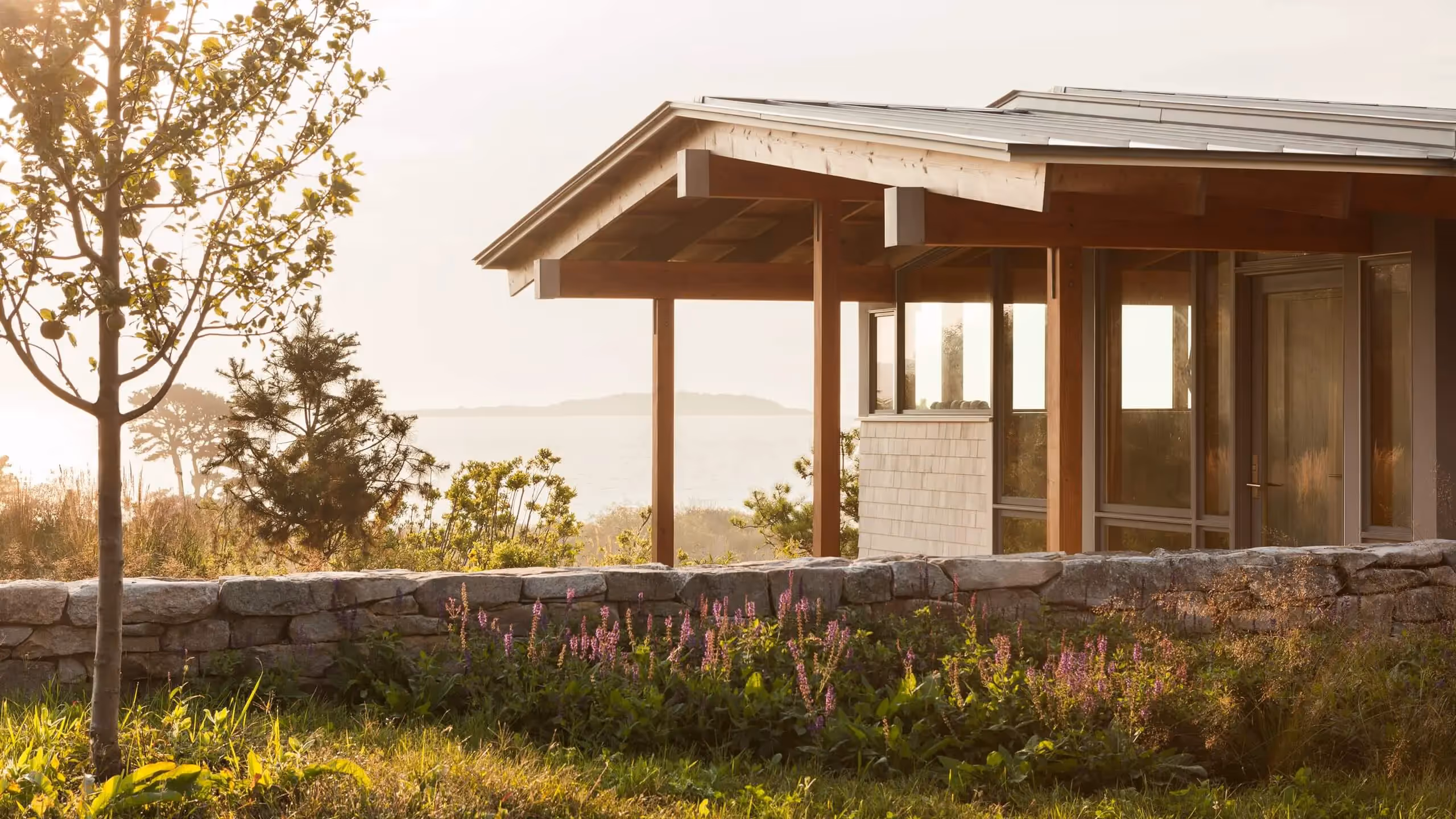 Modern wooden house with stone wall and lavender garden at sunset