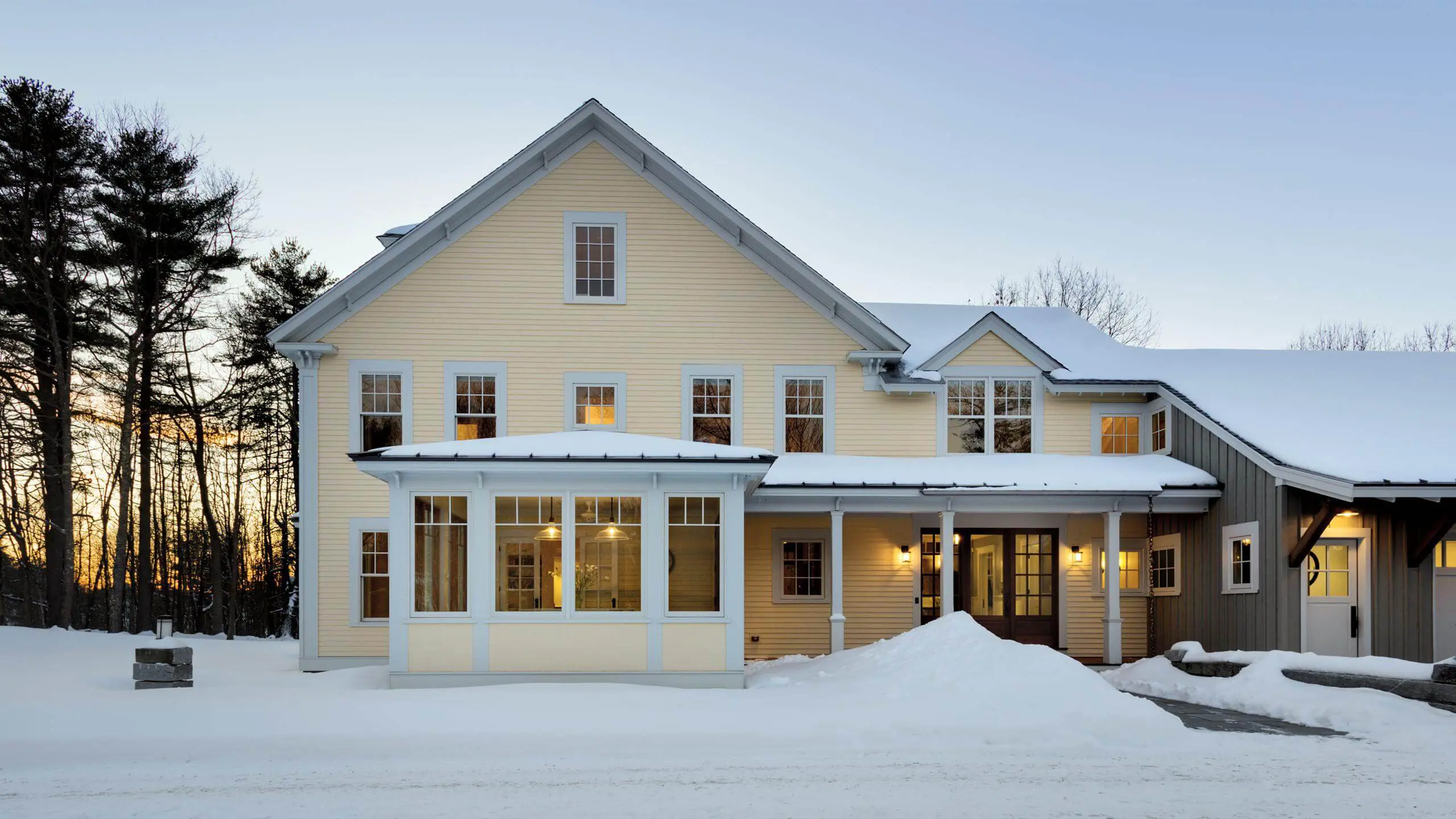 Warm, inviting yellow house with glowing windows in snowy winter landscape